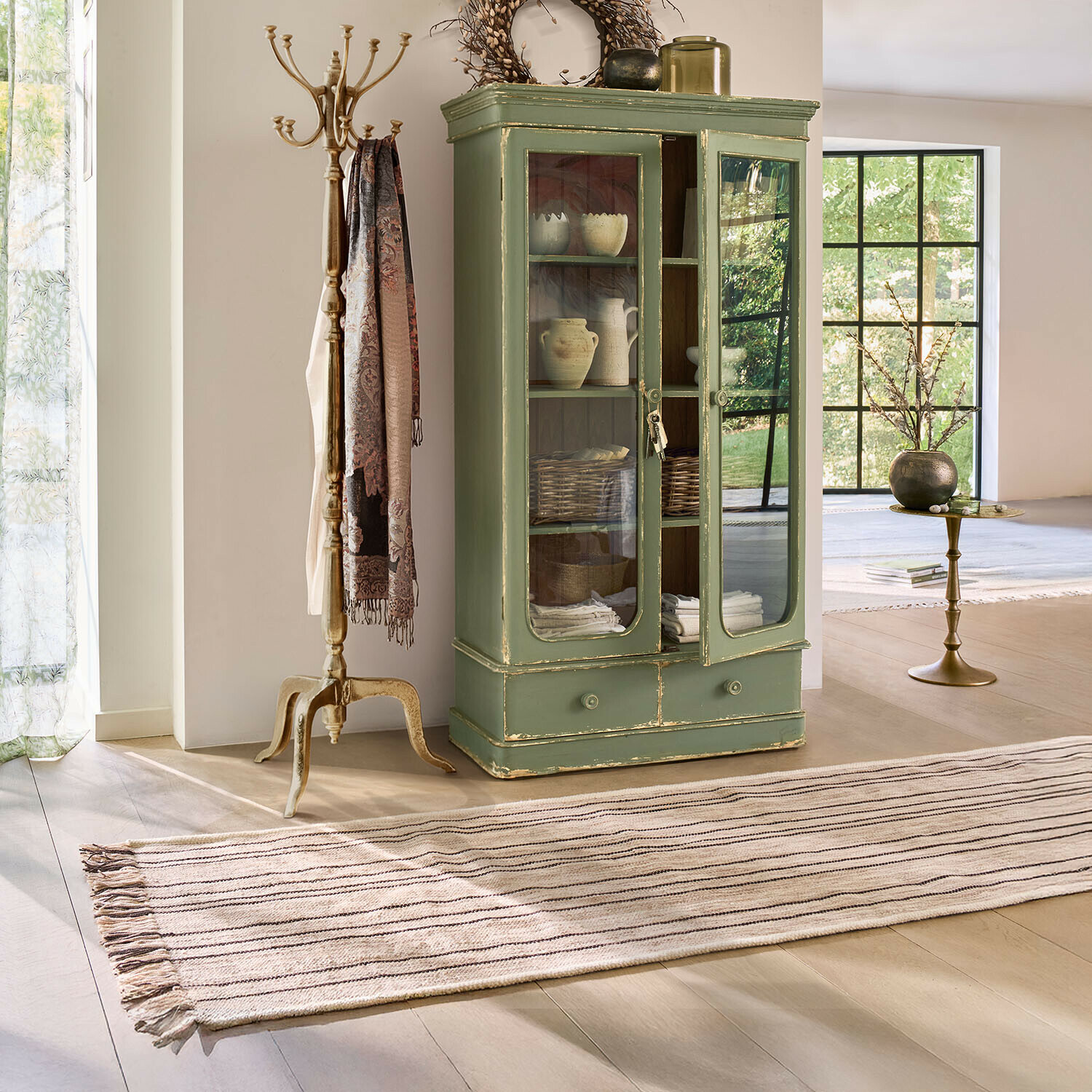 Loper Brisalda Groene houten vitrinekast met glazen deuren en lade in lichte vintage woonkamer