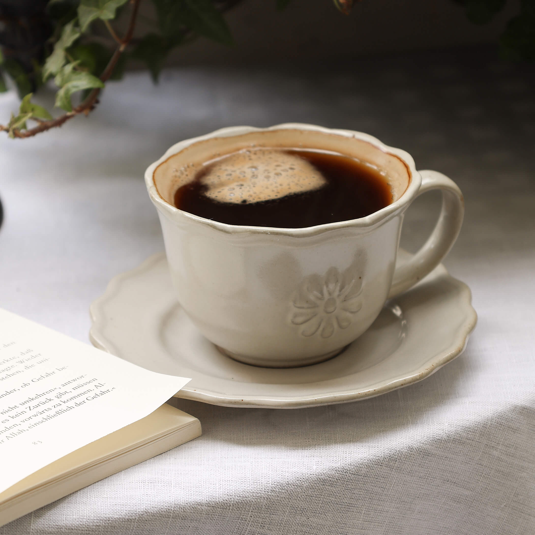 Tasse en céramique beige avec café sur une soucoupe sur une nappe blanche à côté d'un livre ouvert