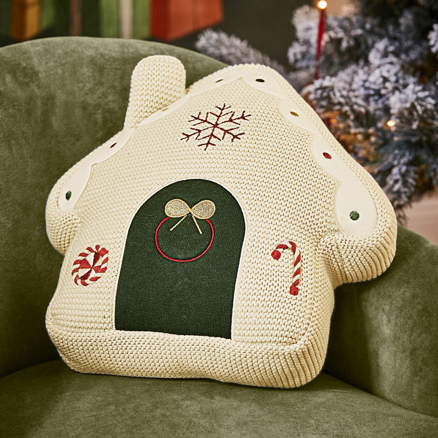 Maison en pain d’épices en tissu Skavari Coussin décoratif en forme de maison tricotée crème avec motifs de Noël et détails verts sur fauteuil vert