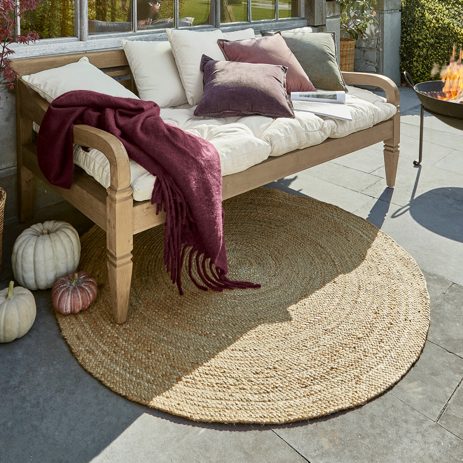 Vloerkleed Imene Ronde jute vloerkleed in natuurlijke kleur onder houten bank met kussens en bordeauxrode deken