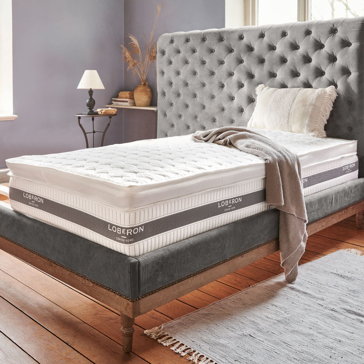 Dekmatras Danisar Grijs gestoffeerd bedframe met wit Loberon-matras en beige deken in gezellige slaapkamer