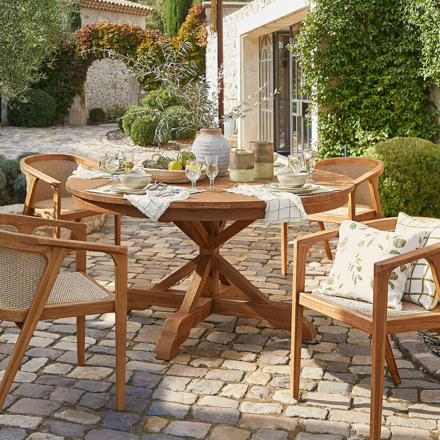 Table Wendreau Table ronde et chaises en teck sur patio pavé avec décorations et vaisselle pour repas en extérieur
