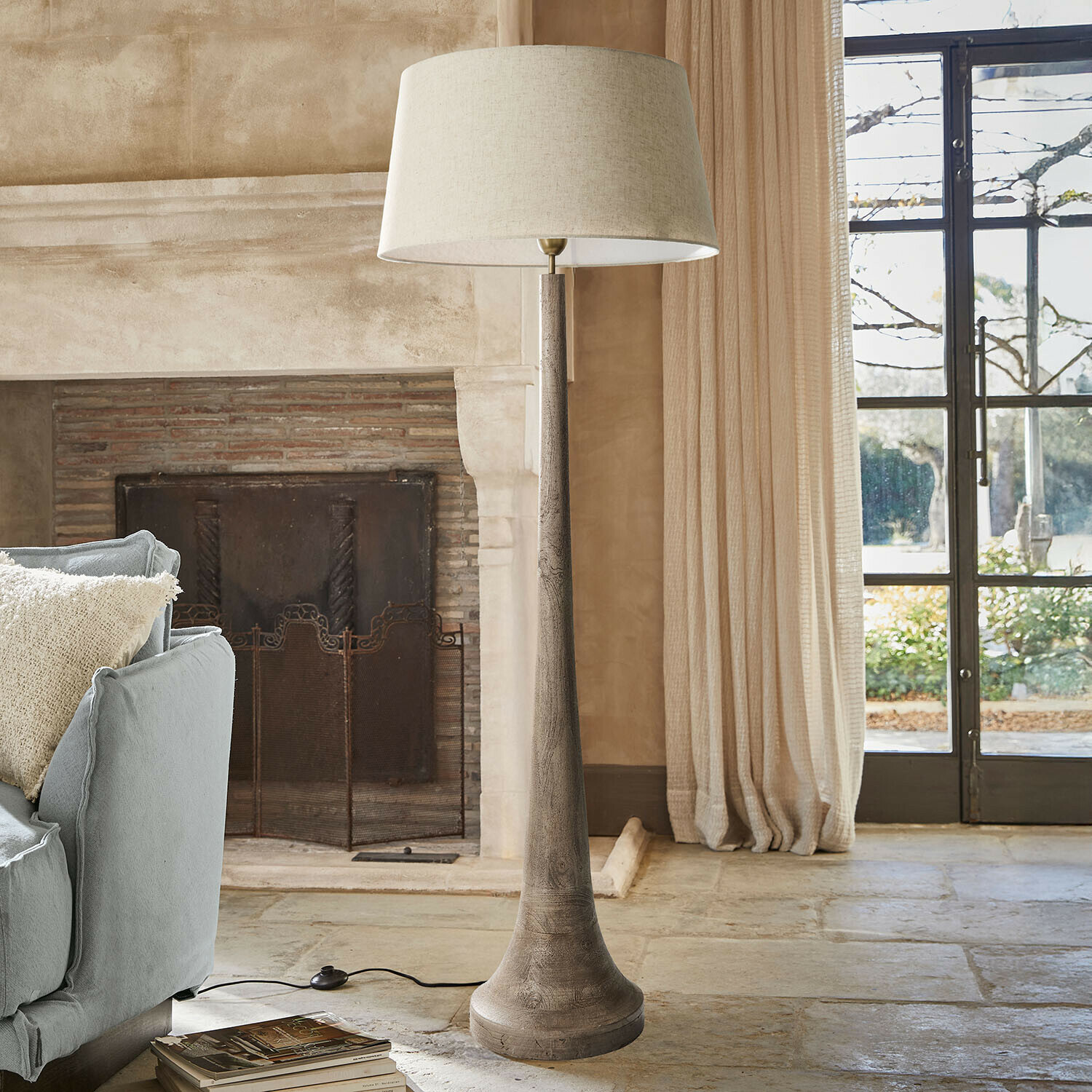 Staande lamp met houten voet en beige kap in een gezellige woonkamer met open haard en bank