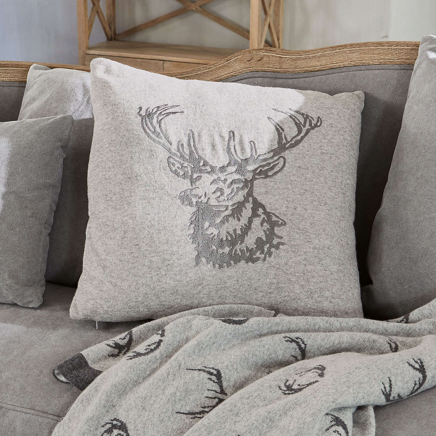 Coussin gris en tissu doux avec motif cerf sur canapé gris avec plaid assorti à motif cerf