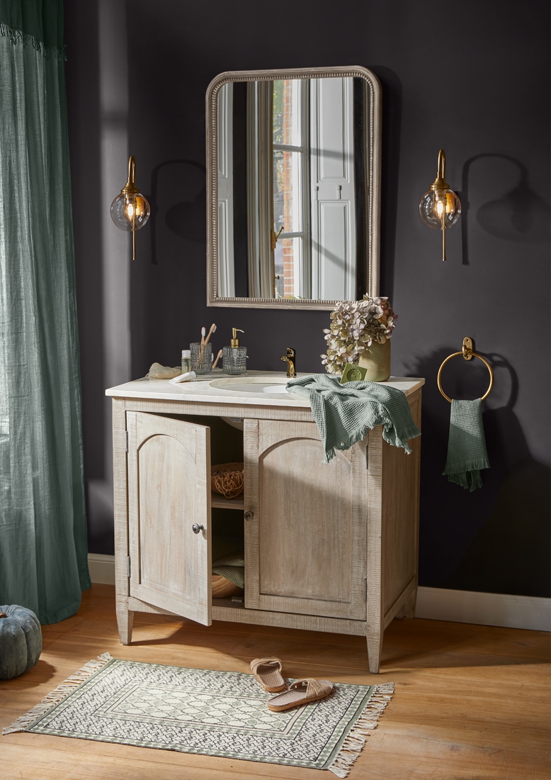 Badmeubel van licht hout met spiegel, gouden accenten en groene handdoek in vintage stijl