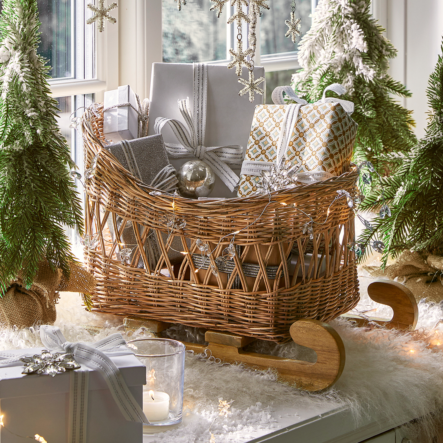 Luge en osier avec patins en bois remplie de cadeaux emballés en argent et blanc pour décoration de Noël