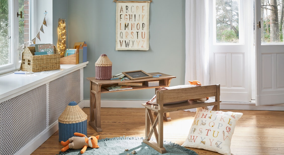 Bureau et banc en bois dans une chambre d'enfant avec coussin et affiche alphabet aux couleurs pastel