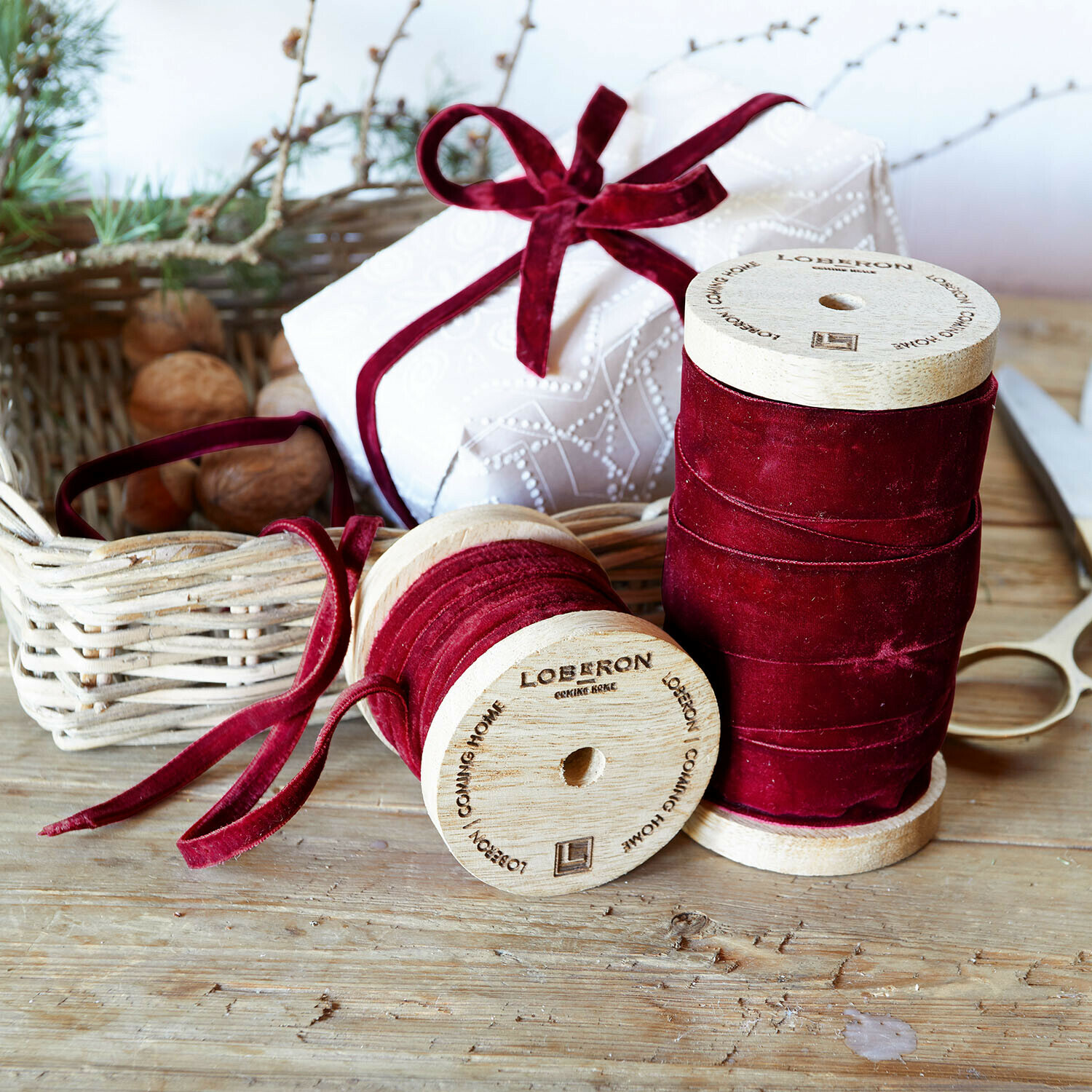 Fluwelen lint set van 2 Liandis Twee houten spoelen met bordeauxrode fluwelen lint op houten tafel met schaar en cadeau