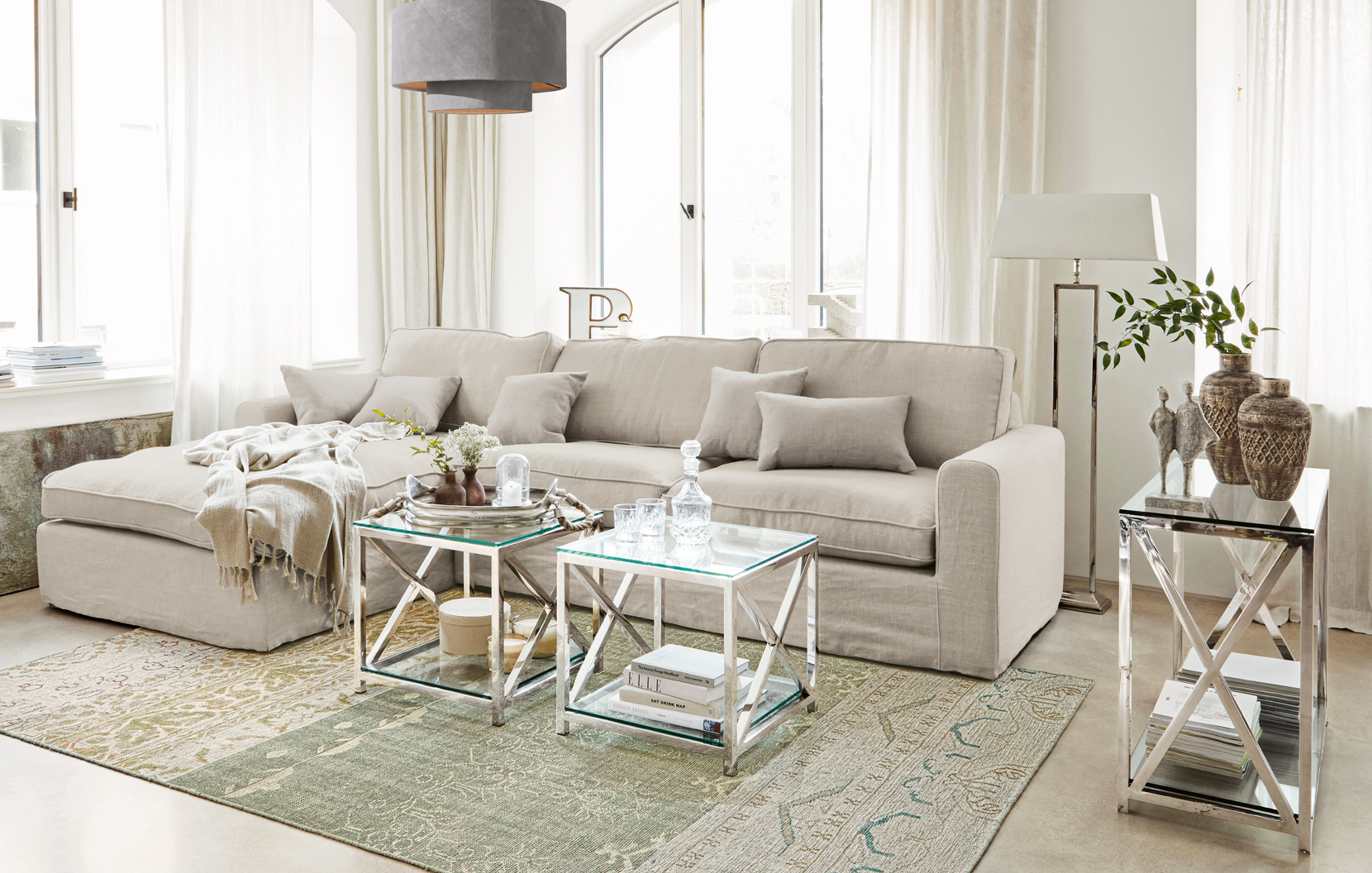 Canapé classique beige en lin avec coussins et tables basses en verre sur cadre métallique dans un salon lumineux