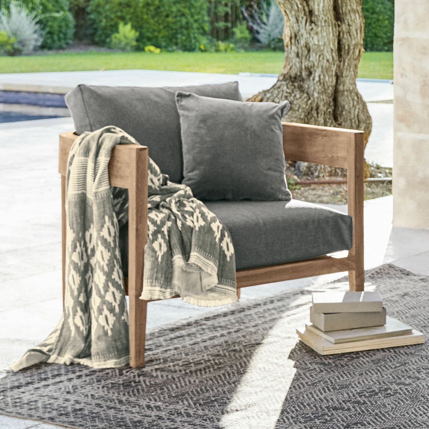 Fauteuil Courtelevant Fauteuil en bois avec coussins gris et plaid à motifs, installé en extérieur sur tapis
