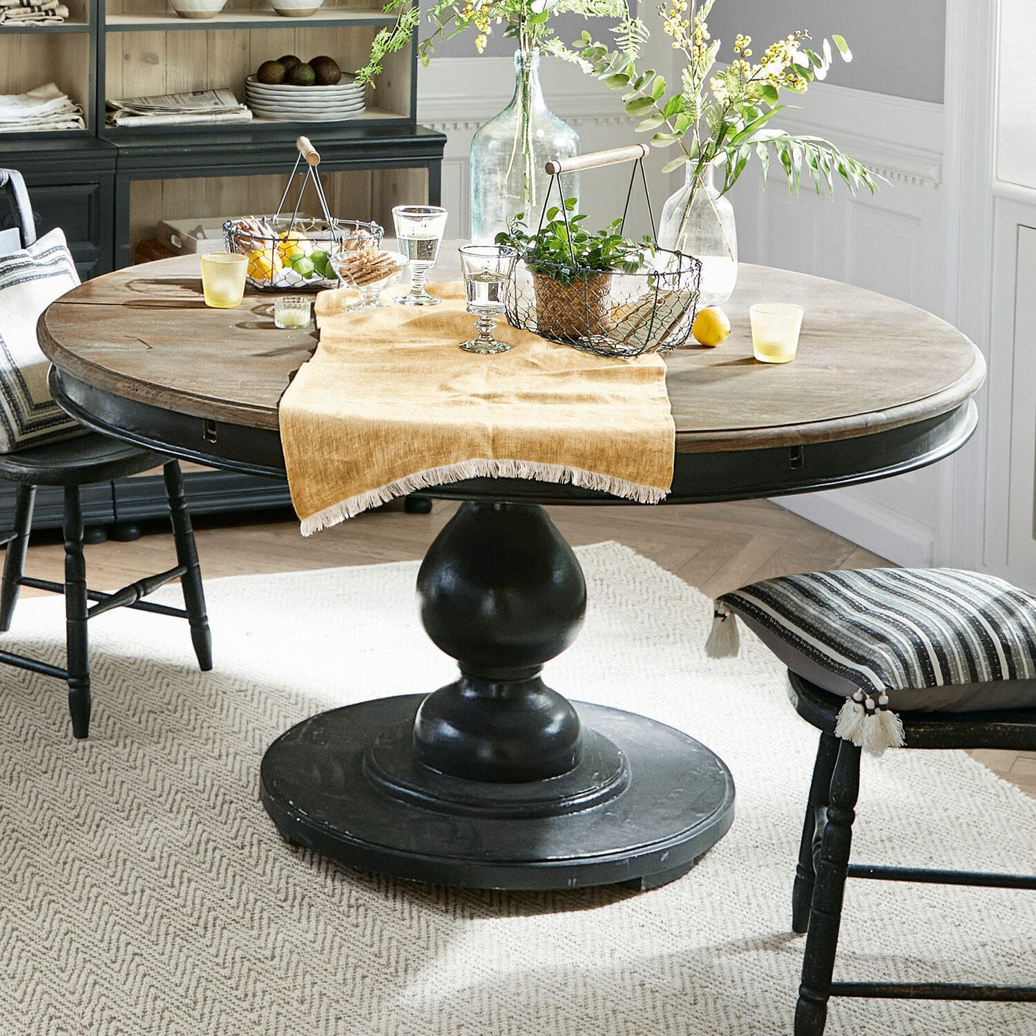 Tafel Shrewsbury Ronde houten tafel met zwarte voet en decoratie op beige loper in eetkamer