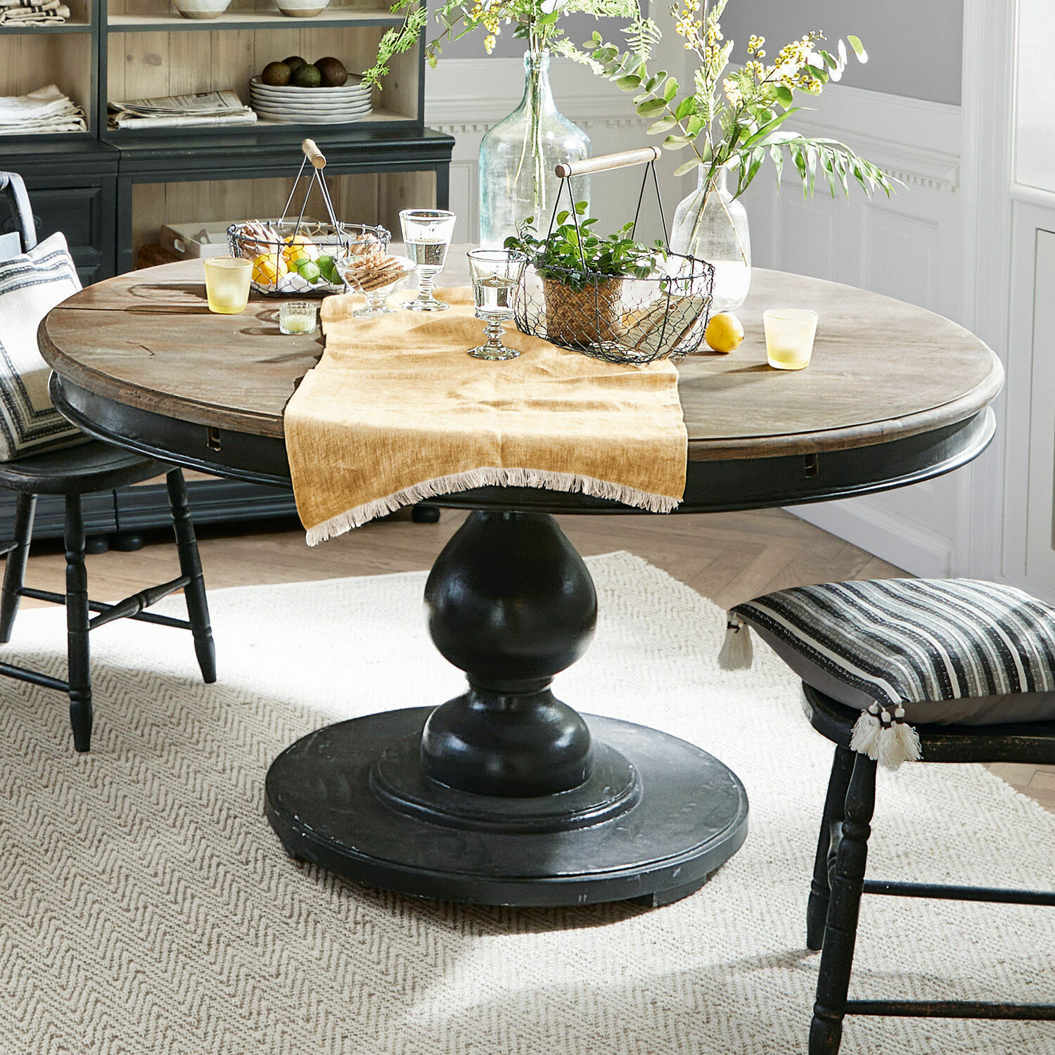 Table Shrewsbury Table ronde en bois avec pied noir et décorations sur nappe beige dans une salle à manger