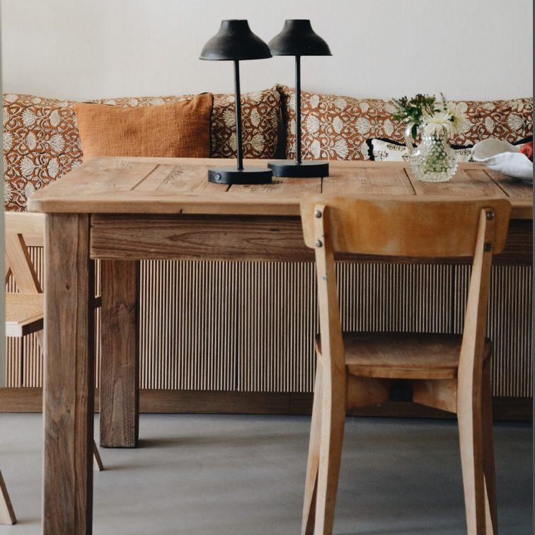 Table en bois avec deux lampes noires et un vase de fleurs devant un canapé avec coussins orange
