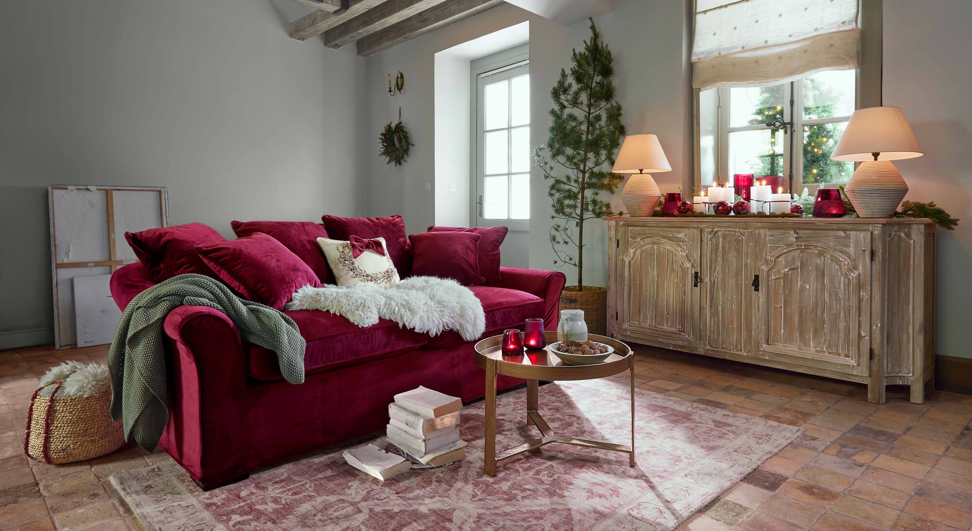 Canapé en velours rouge avec coussins et plaid vert dans un salon chaleureux avec buffet en bois et décorations de Noël