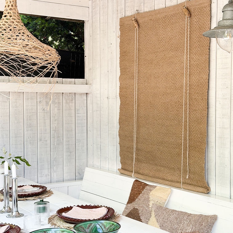 Mur en bois blanc avec store en jute naturel et table décorée avec coussins dans un style bohème