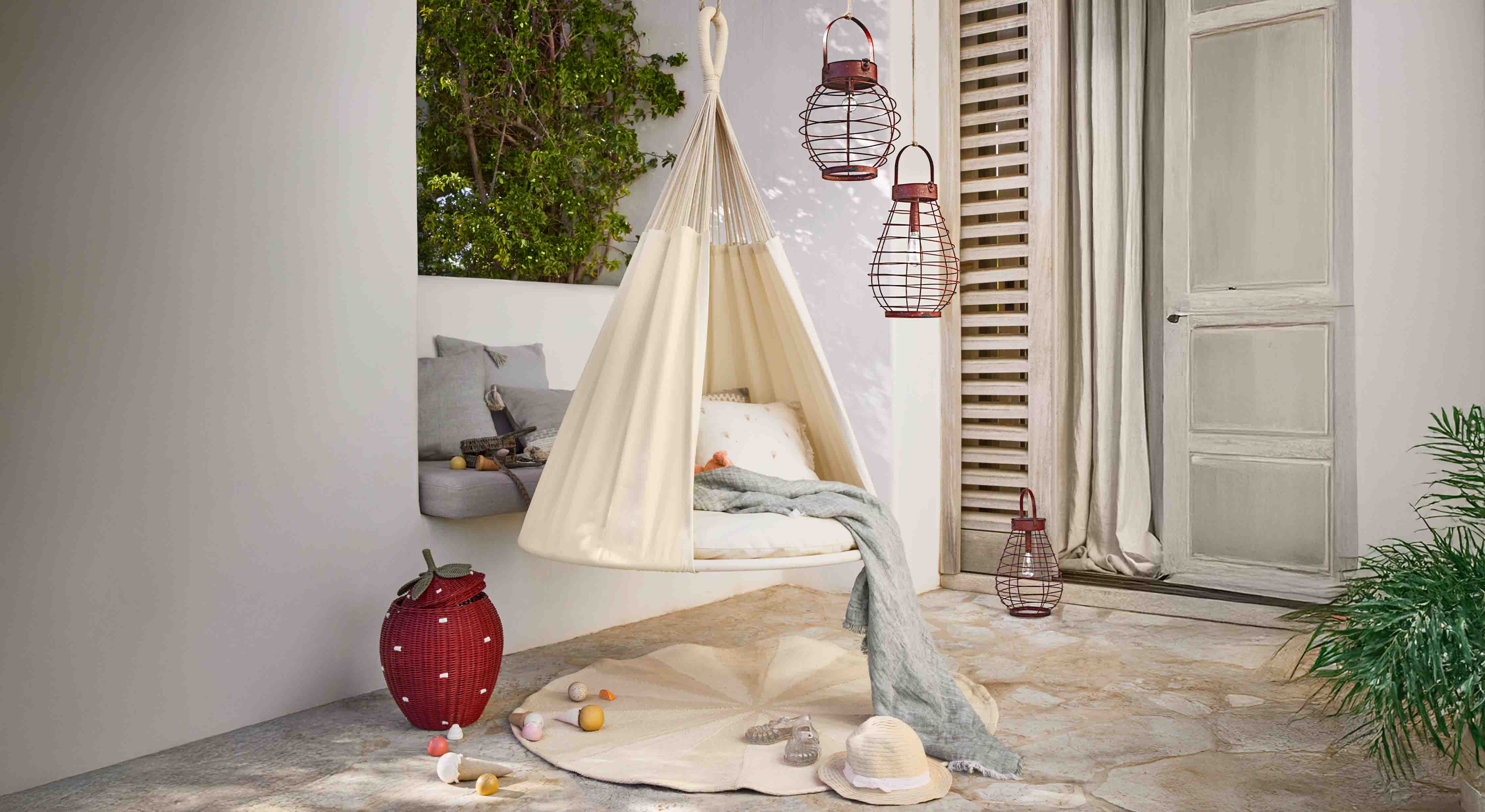 Beige hangende stoffen stoel op terras met kussens en decoratieve metalen lantaarns