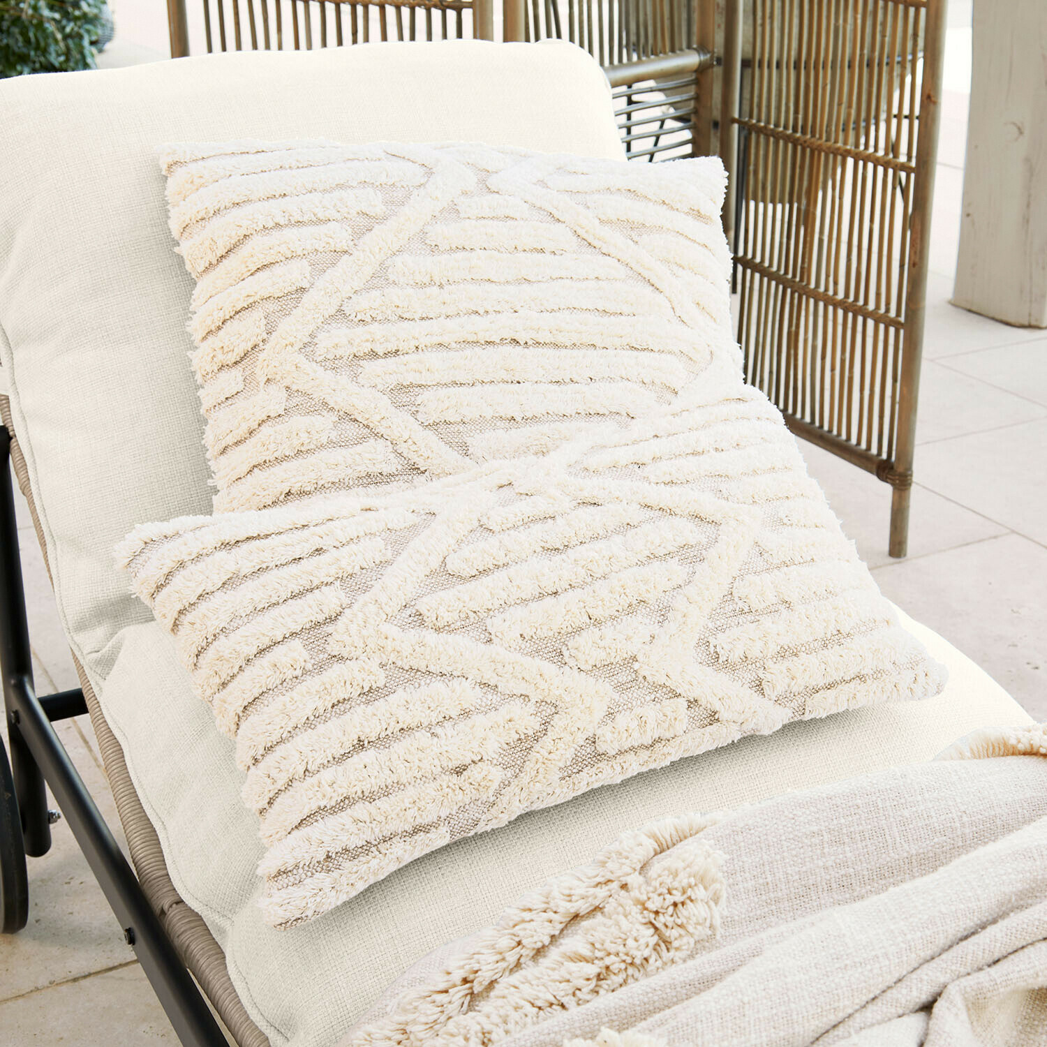 Twee crèmekleurige sierkussens van zacht materiaal met geometrisch patroon op een lichte ligstoel