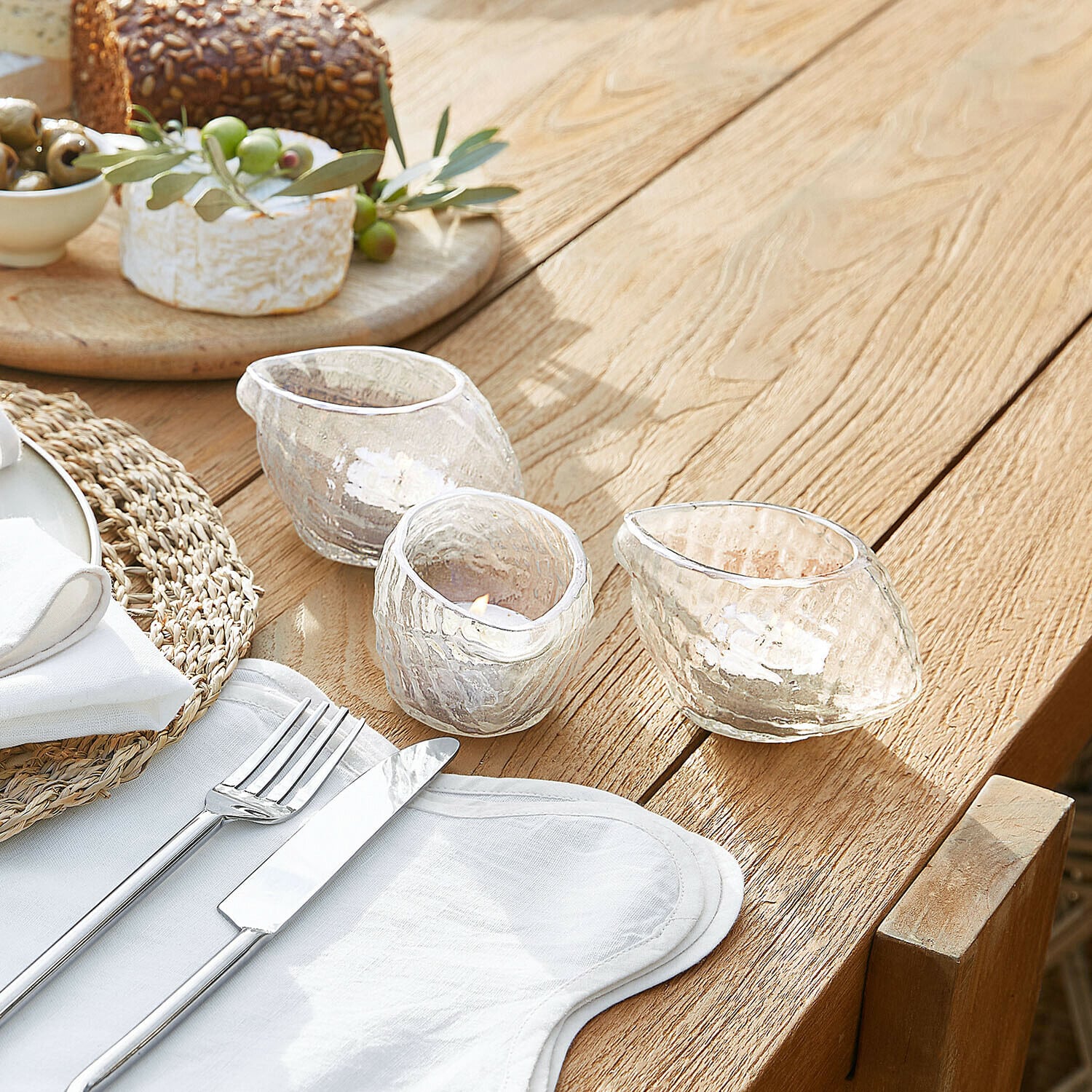 Trois photophores en verre transparent aux formes irrégulières sur une table en bois avec couverts
