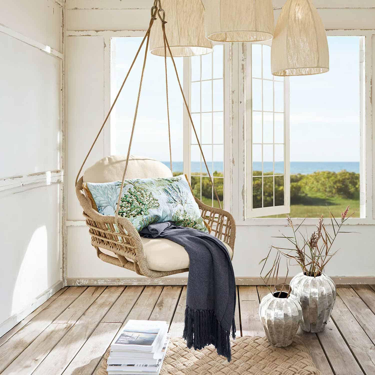 Hangstoel van riet met crème kussen en blauwe deken in lichte kamer met zeezicht