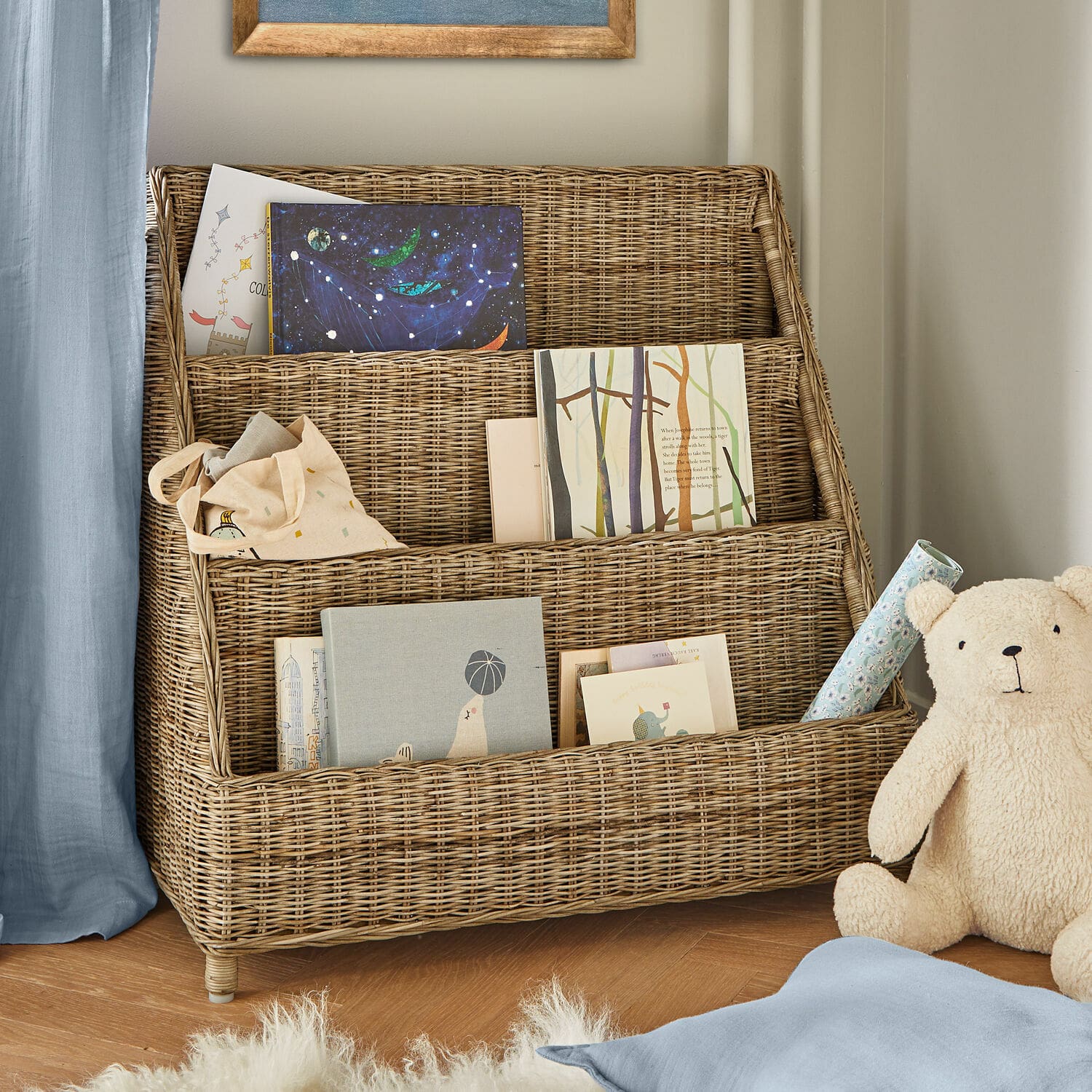Bibliothèque Trésolia Étagère à trois niveaux en rotin naturel avec livres et ours en peluche dans une chambre d'enfant
