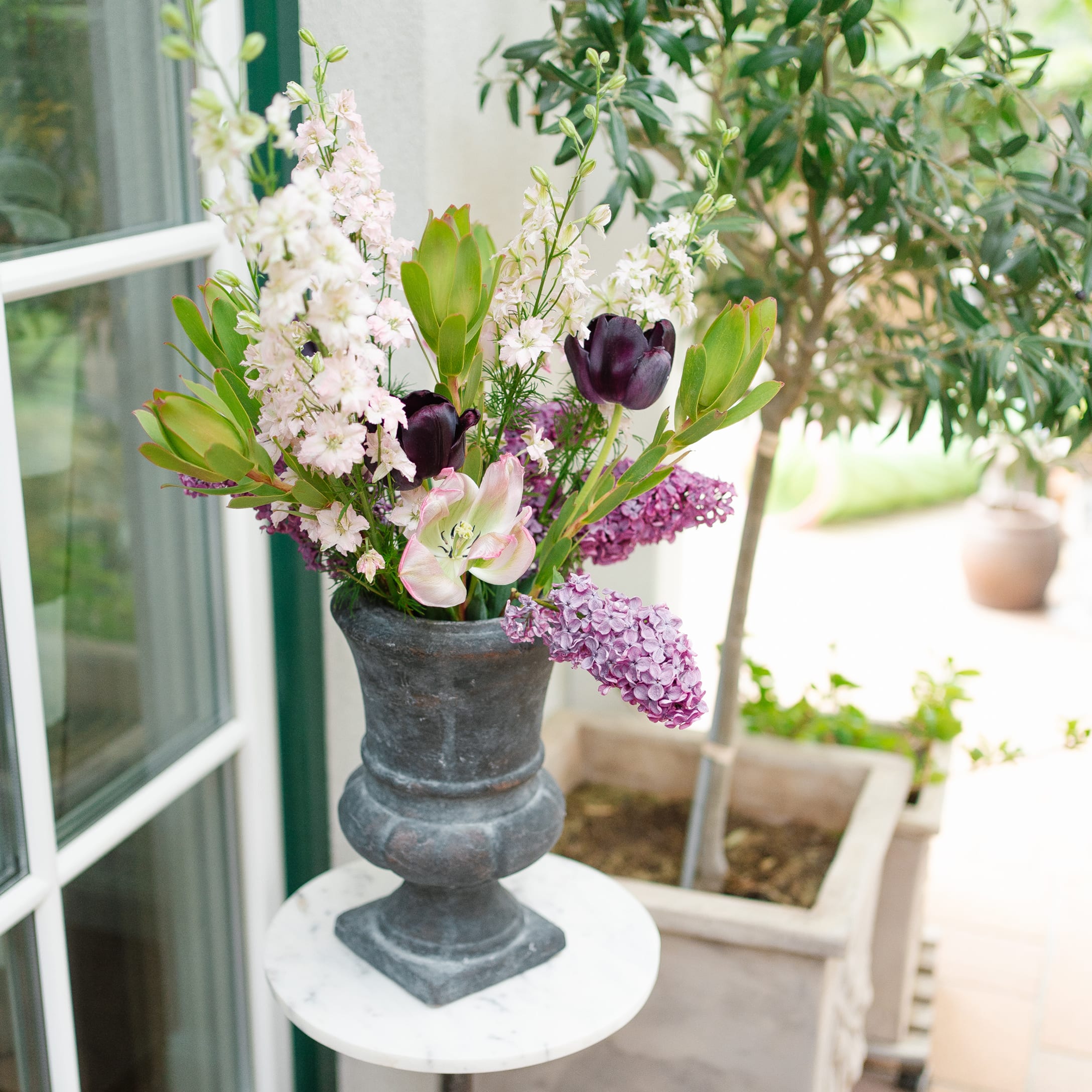 Vase décoratif en pierre grise foncée avec bouquet de fleurs roses et violettes sur une table ronde