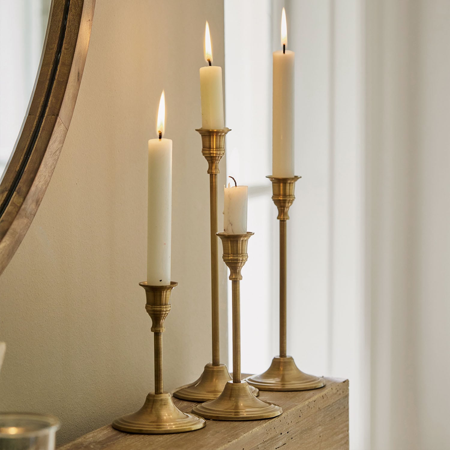 Ensemble de quatre bougeoirs en laiton avec bougies blanches sur une étagère en bois dans un intérieur lumineux