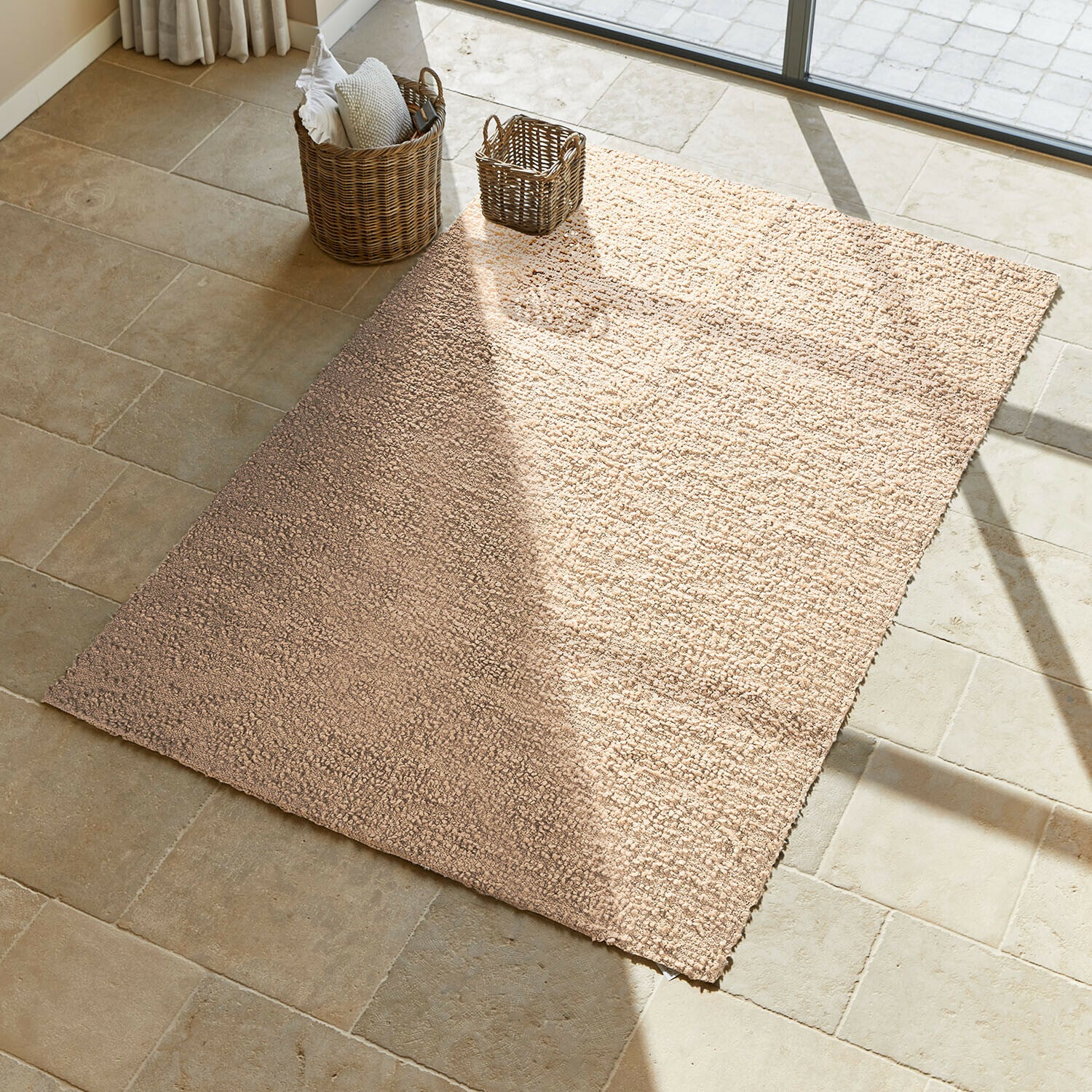 Tapis Wodaha Tapis beige en matériau doux sur sol en pierre claire avec paniers en osier à côté