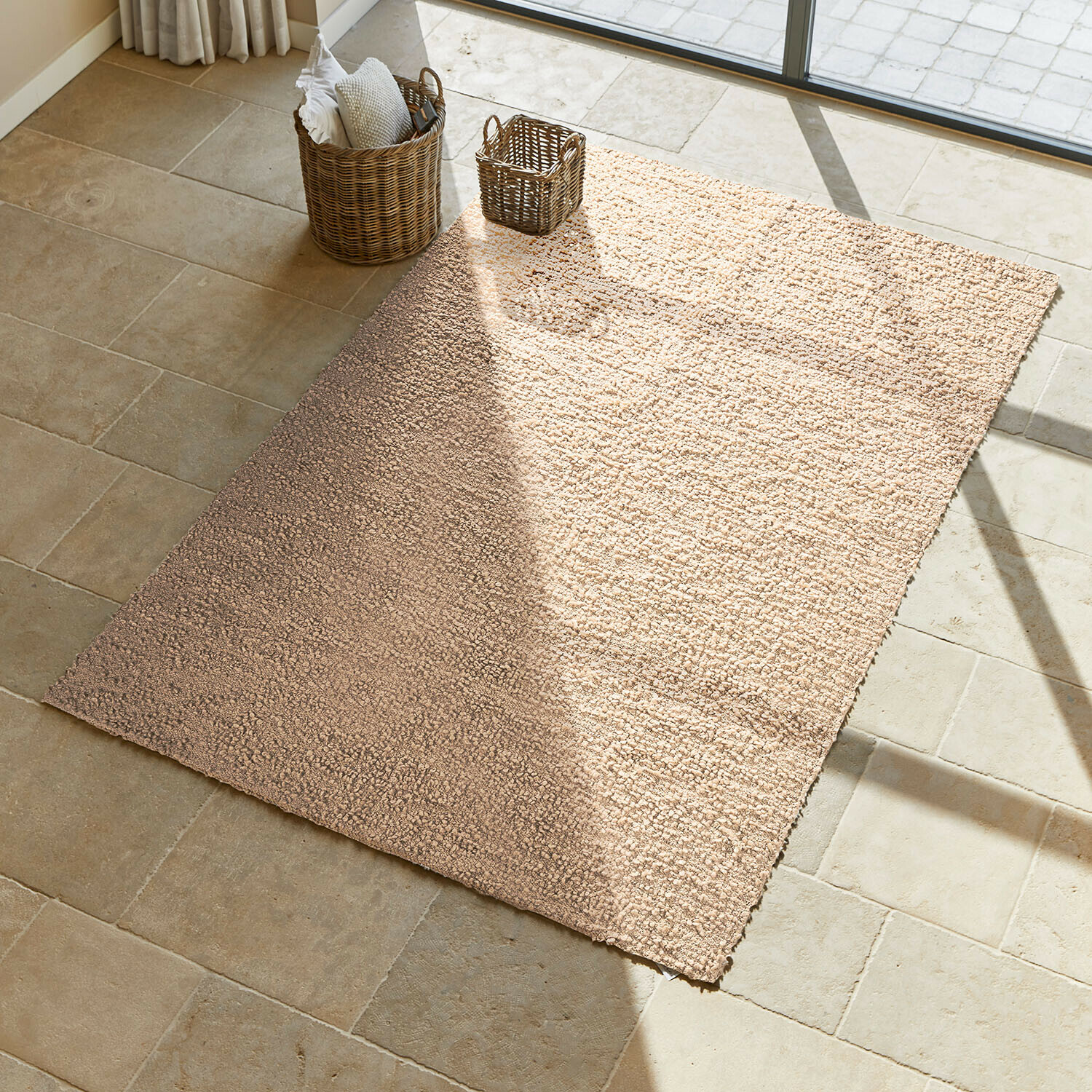 Tapis Wodaha Tapis beige en matériau doux sur sol en pierre claire avec paniers en osier à côté