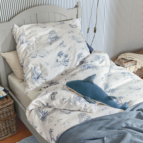 Parure de lit en coton blanc avec motifs marins bleus sur lit gris et coussin décoratif requin