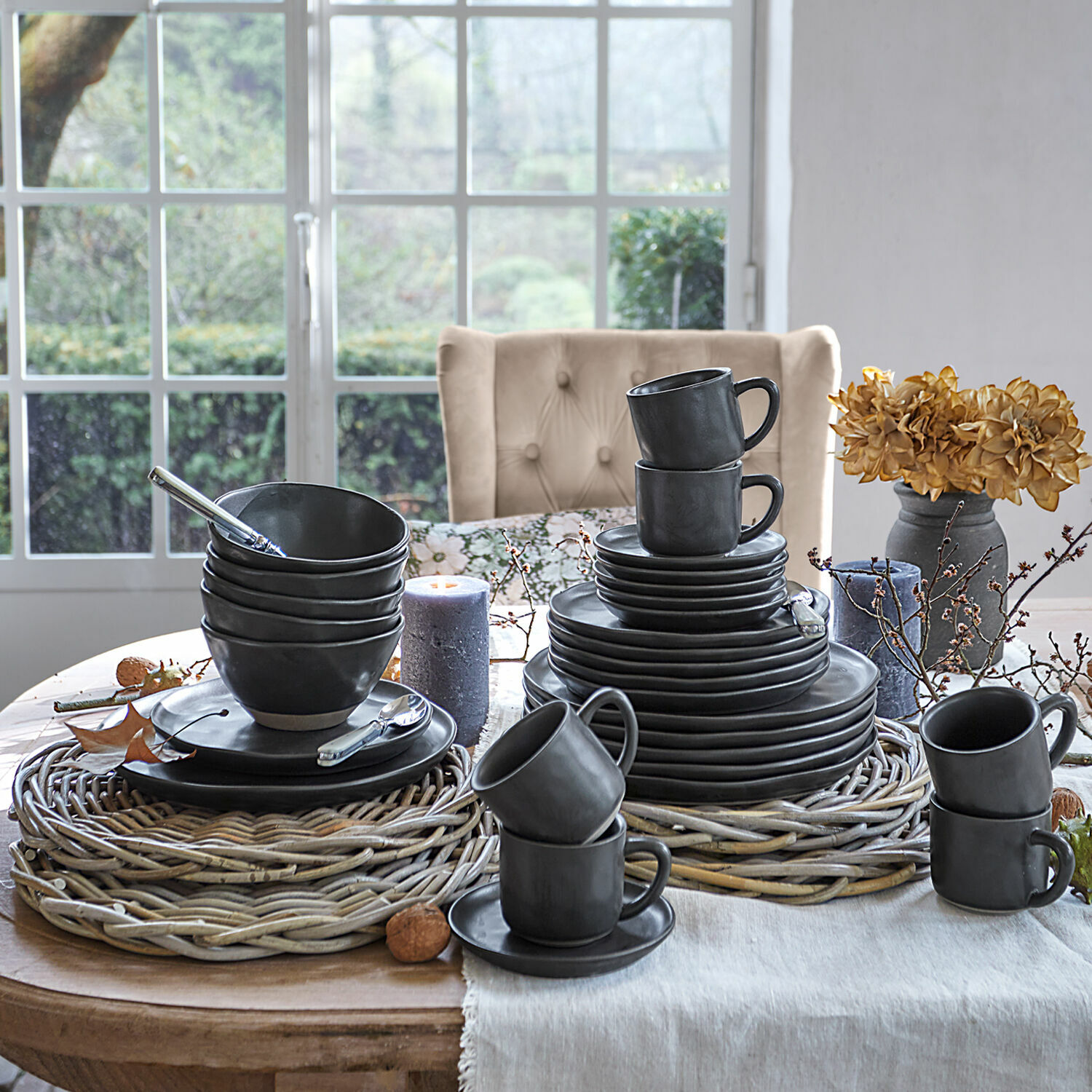 Service 30 pièces (second choix) Bièrre Service de table en céramique noire avec sous-plats en osier sur table en bois décorée près d'une fenêtre