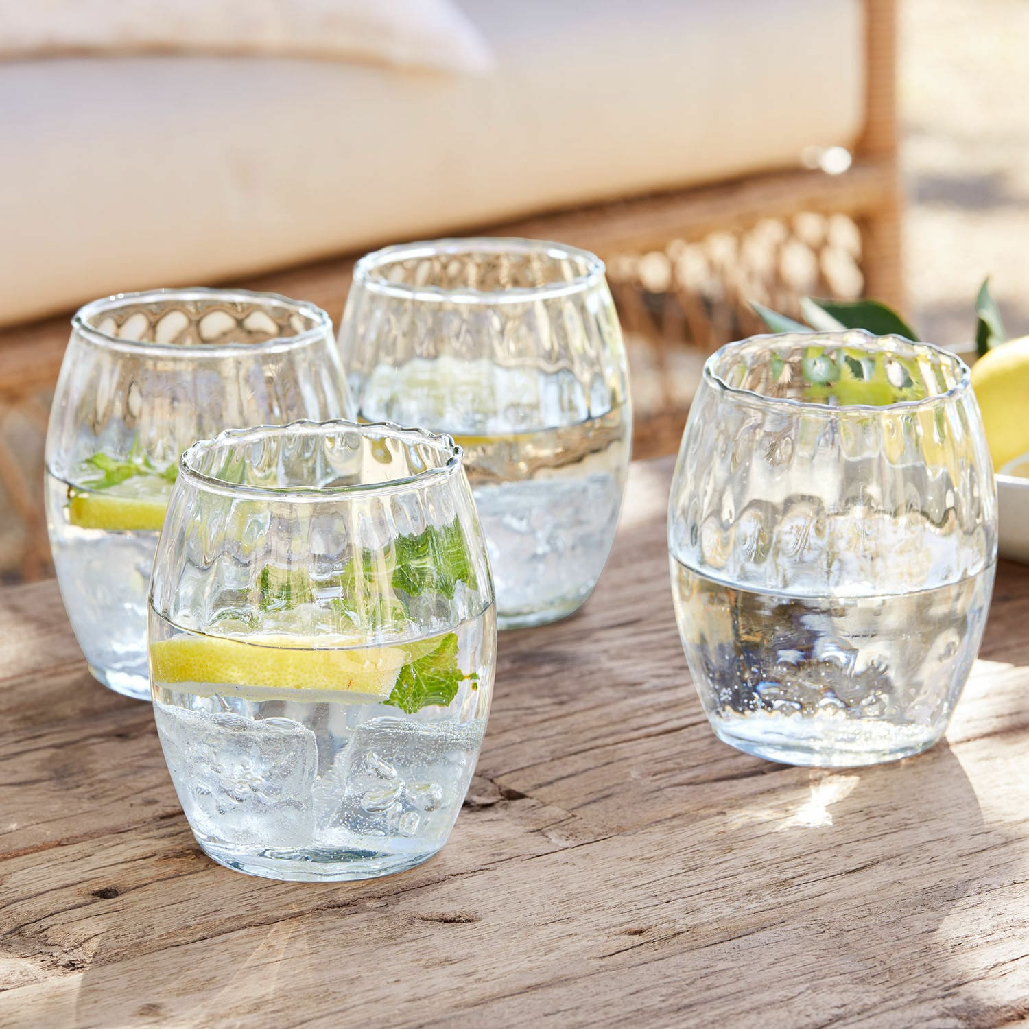 Lot de 4 verres Bourgavin Ensemble de quatre verres en verre transparent avec eau, glace et citron sur une table en bois