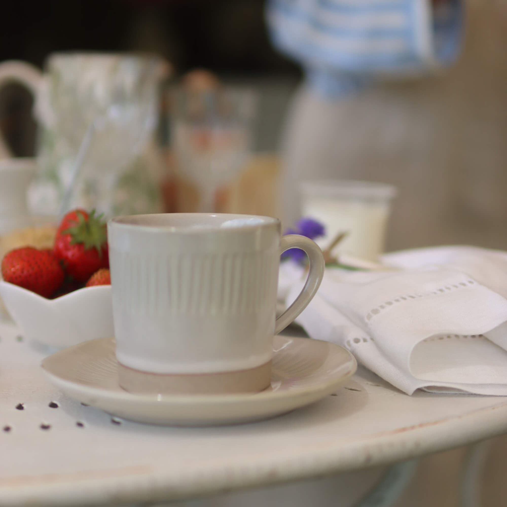 Tasse en céramique beige avec soucoupe sur table blanche avec fraises et serviette en lin