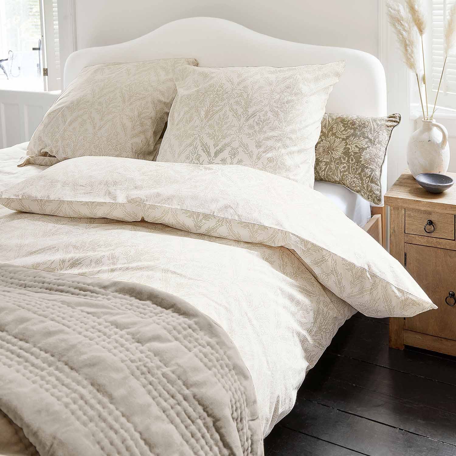 Licht katoenen beddengoed met fijn plantenpatroon en zachte deken in een gezellige slaapkamer