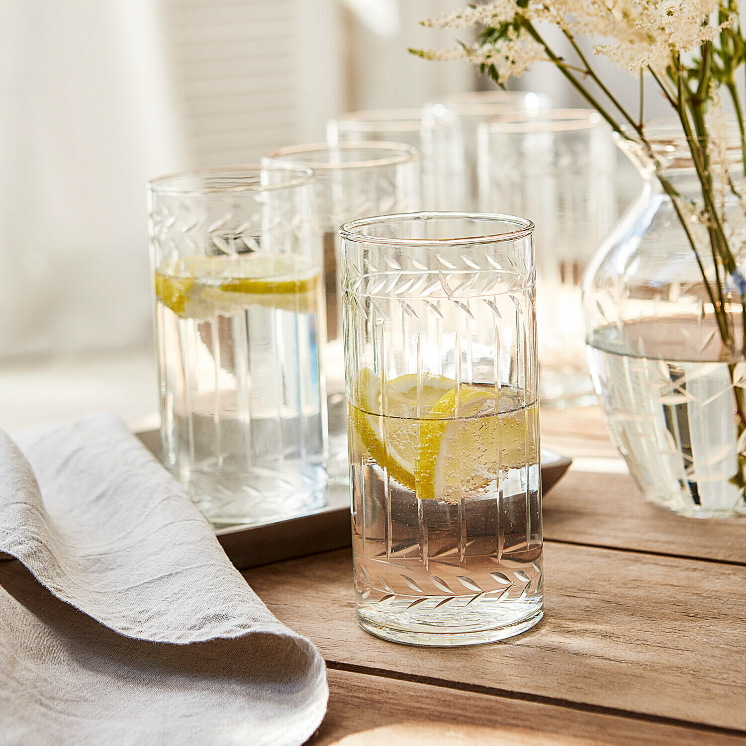 Glas set van 6 Padiès Glazen van helder glas met gegraveerd bladmotief, gevuld met citroenwater op houten tafel