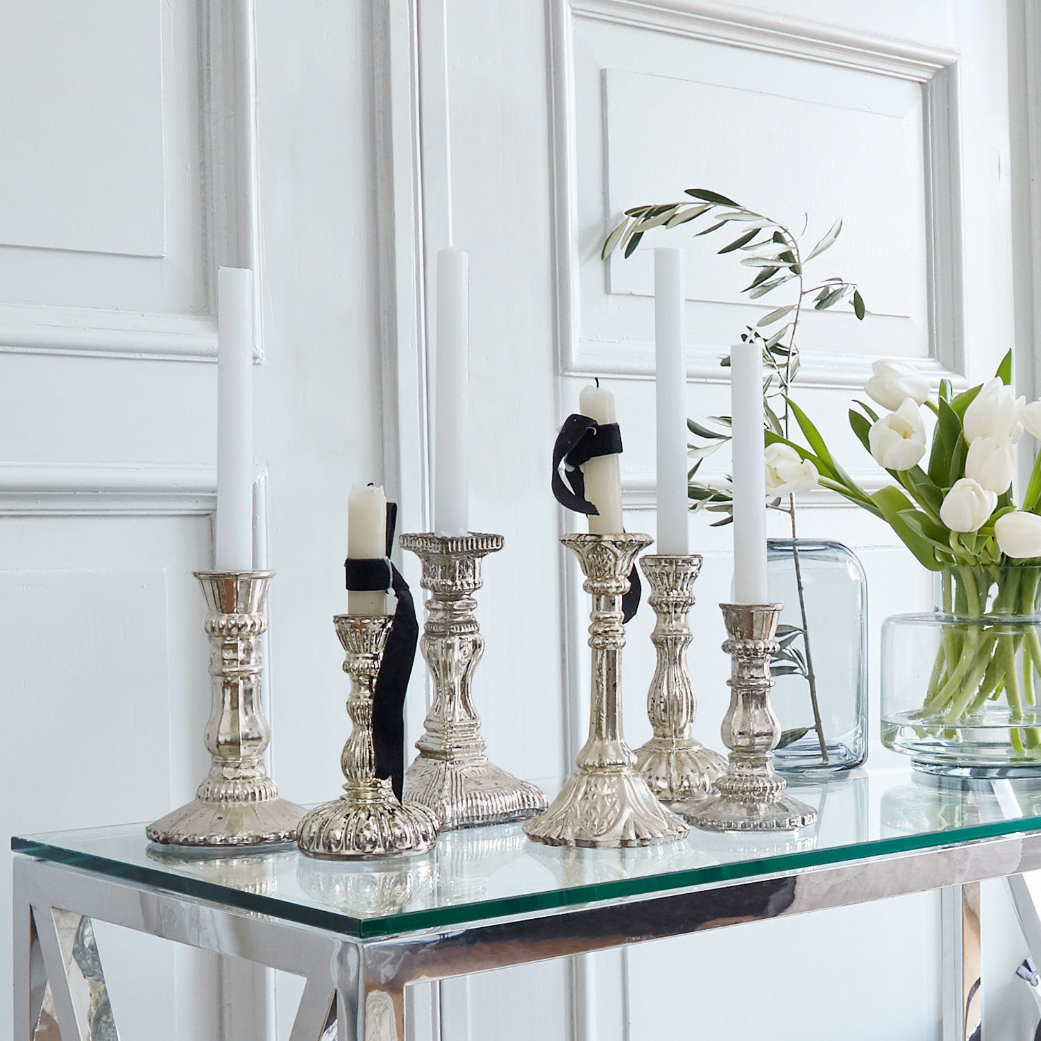 Kandelaar set van 6 Adolpha Set zilverkleurige metalen kandelaars met witte kaarsen op glazen tafel in lichte kamer