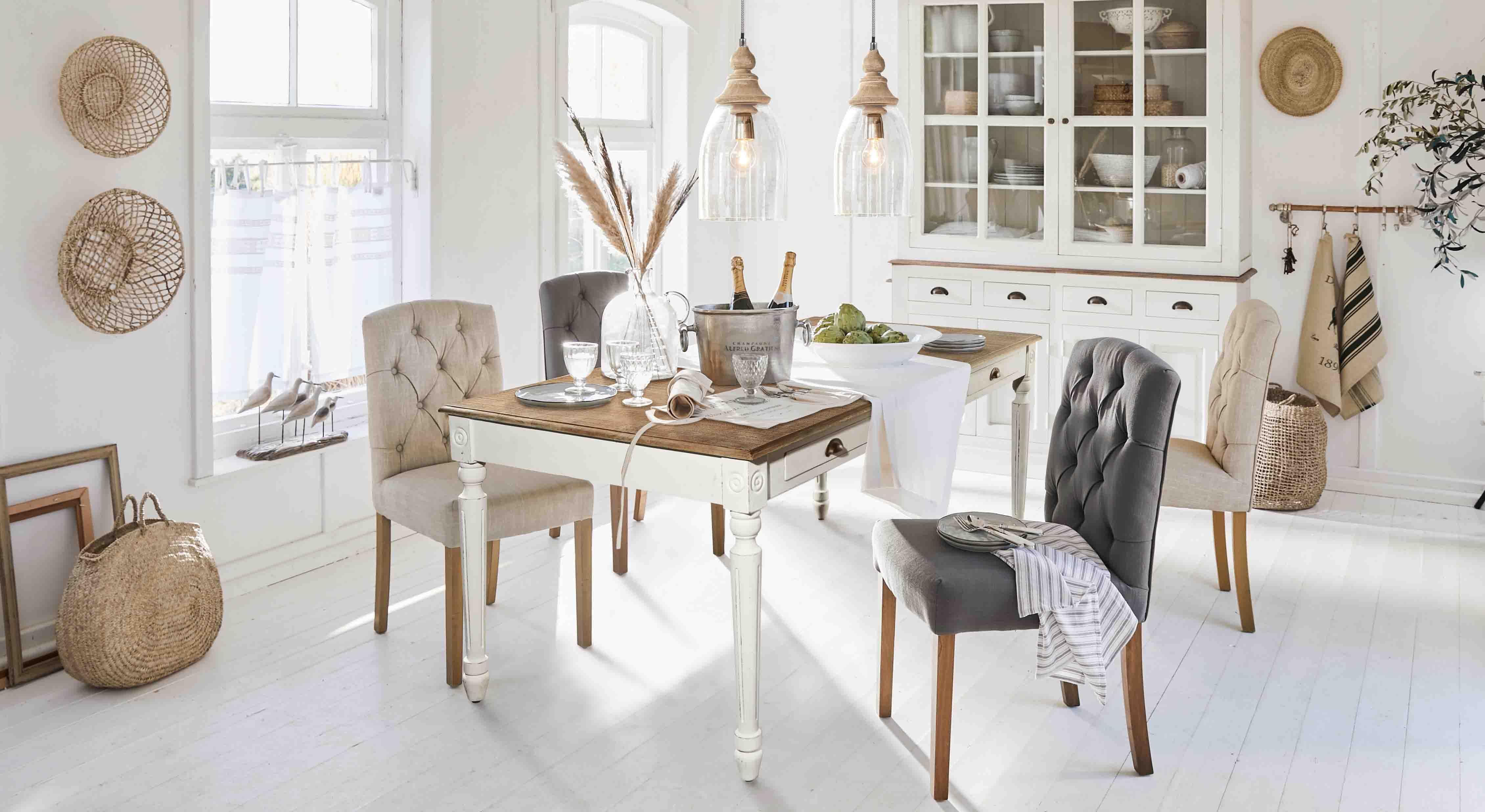 Salle à manger rustique avec table en bois blanc et chaises rembourrées beige et gris clair dans une ambiance lumineuse