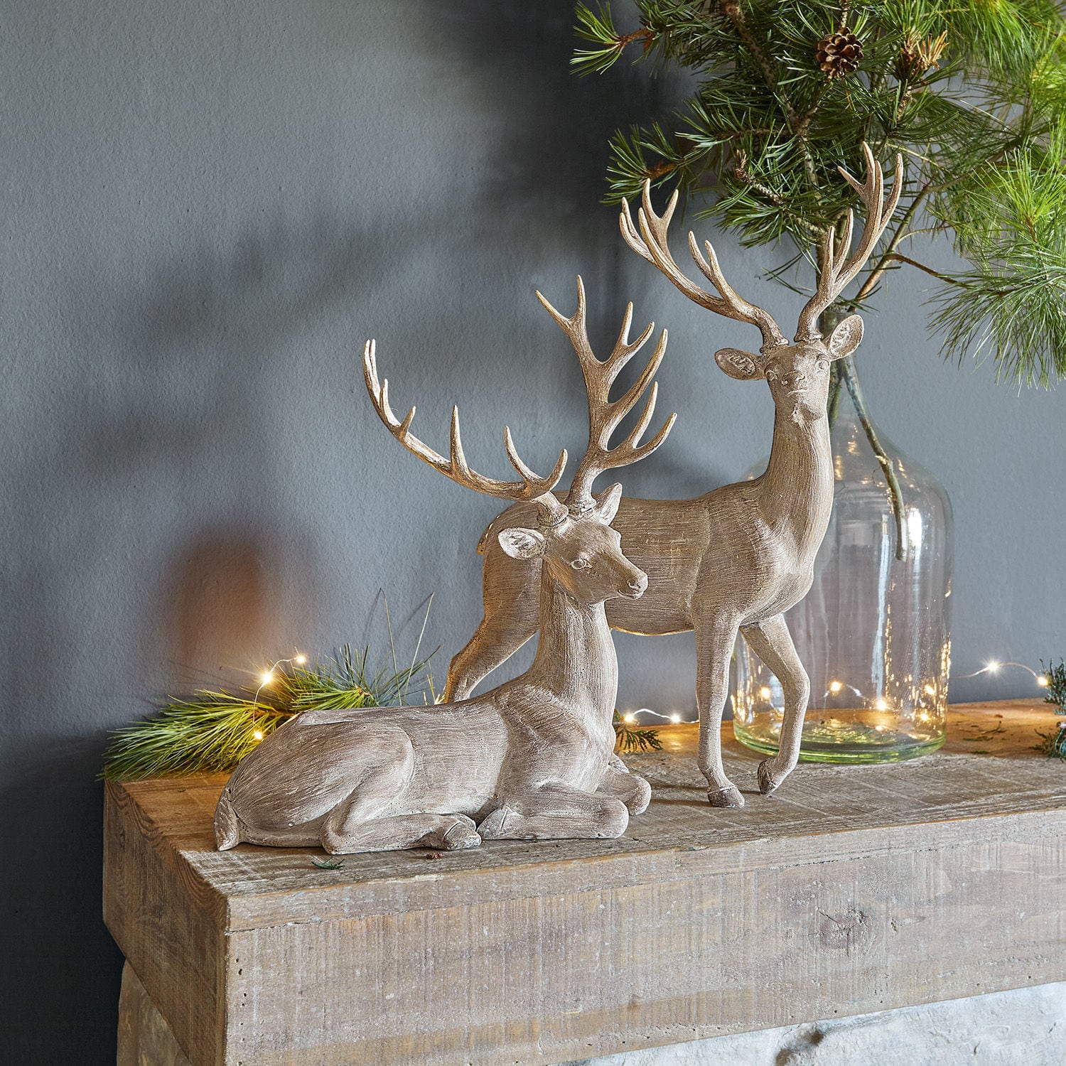 Deux figurines de cerfs en bois couleur naturelle sur une table en bois avec des branches vertes décoratives