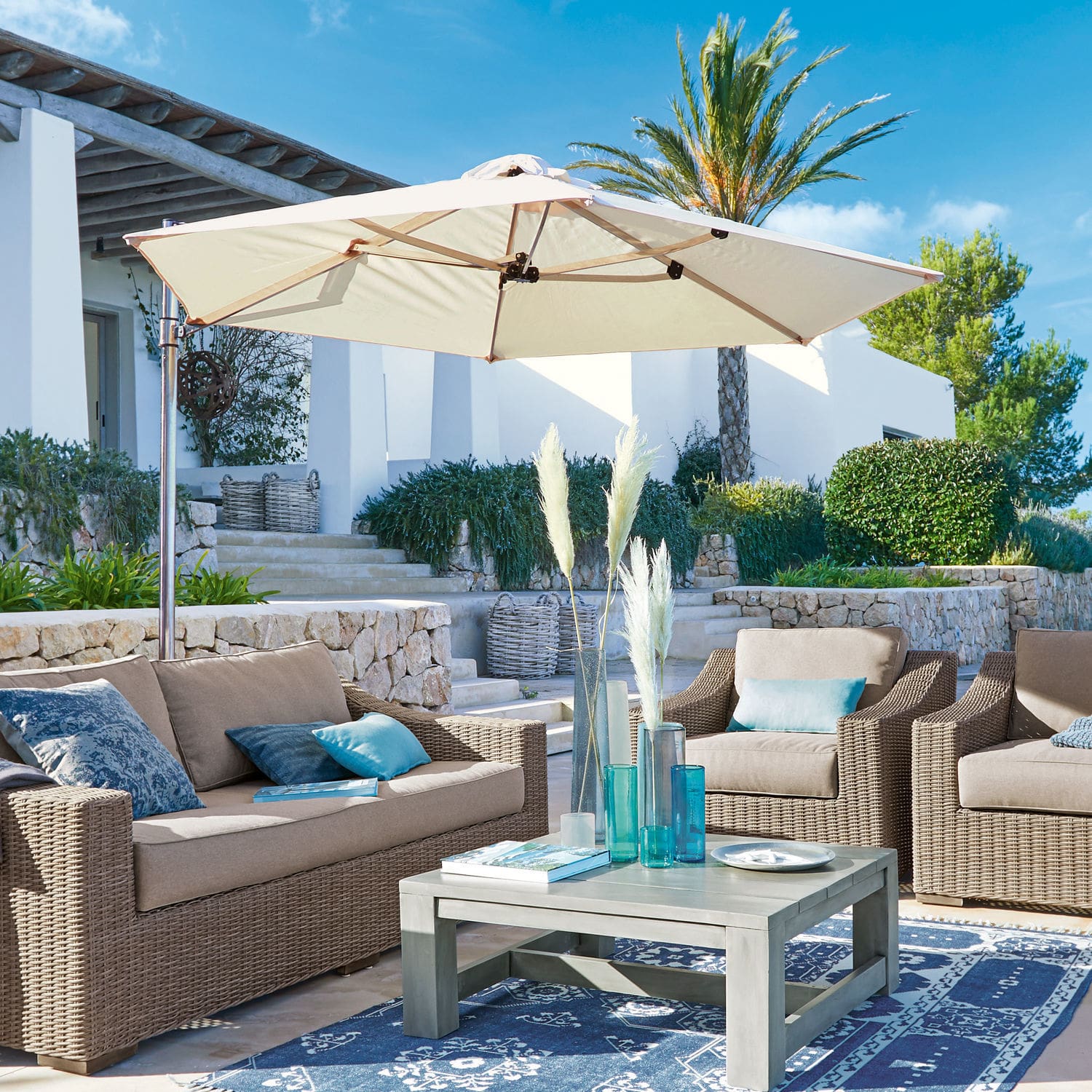 Ensemble de mobilier de jardin en rotin synthétique beige avec parasol crème sur terrasse avec tapis bleu