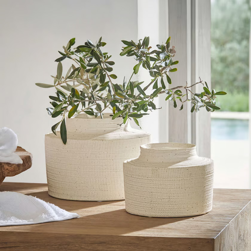 Deux vases en céramique crème texturée posés sur une table en bois avec des branches vertes