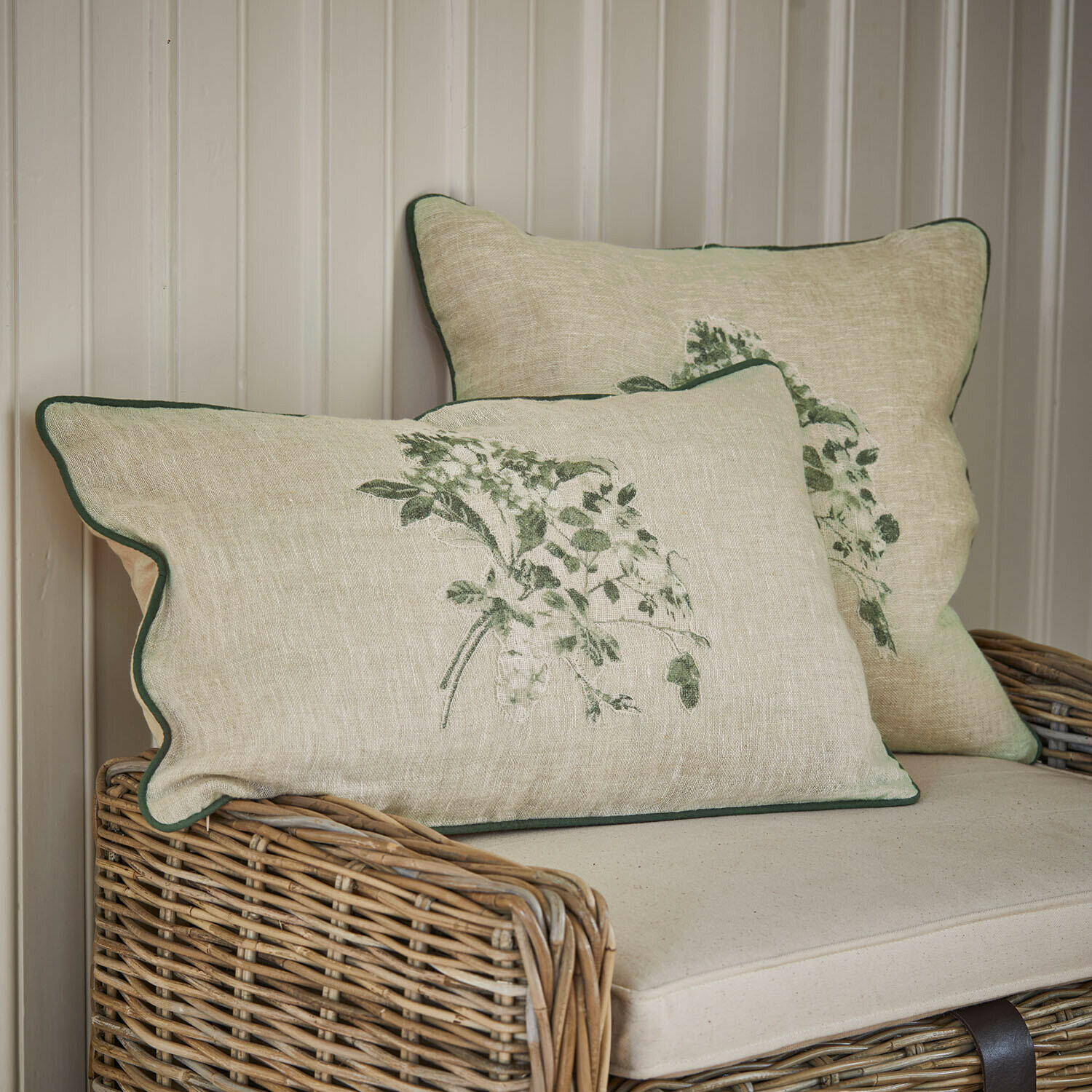 Lot de 2 housses de coussin Chantrelle Coussins en lin beige avec motif végétal vert et bordure verte sur canapé en osier