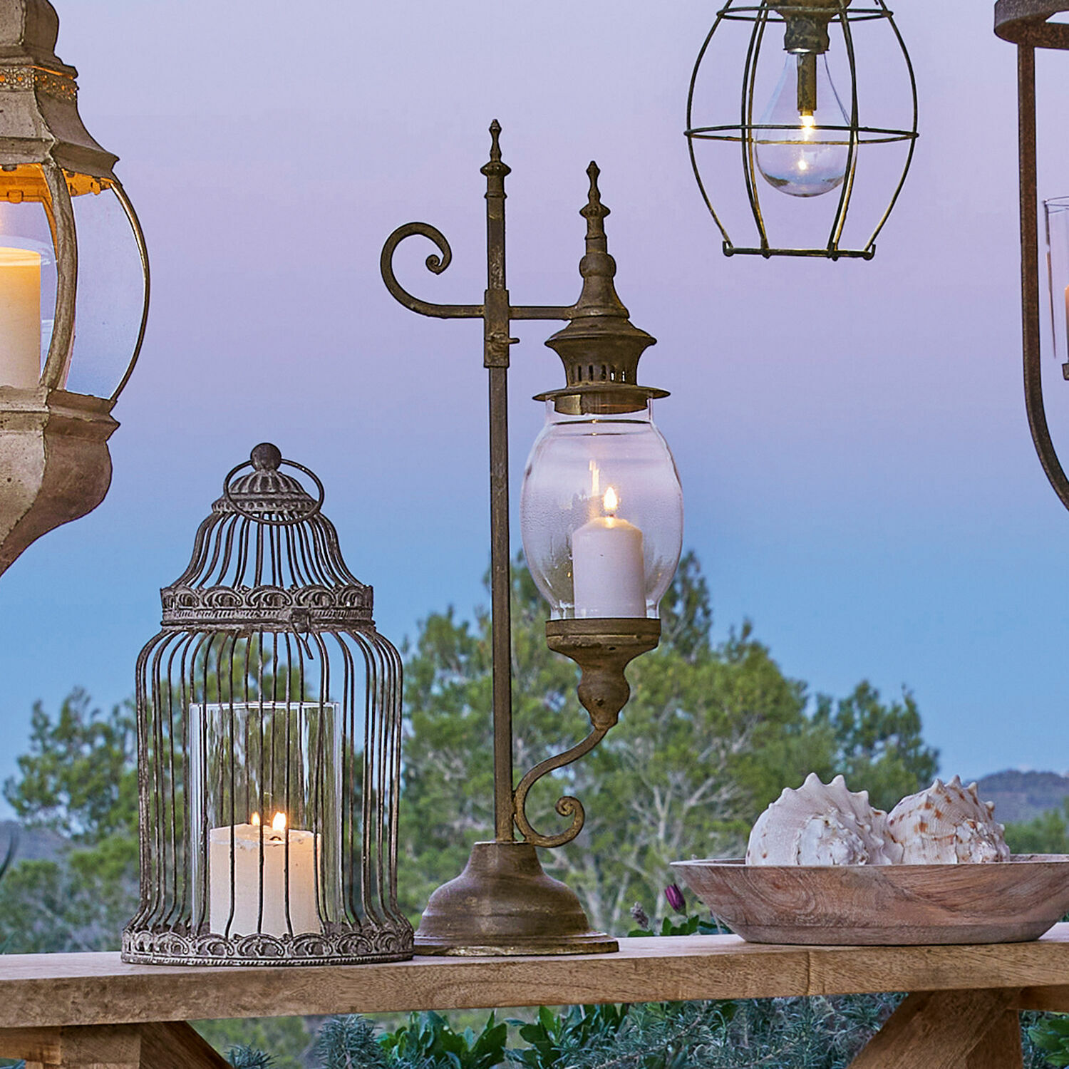 Lantaarn Bowral Metalen lantaarn met helder glas en brandende kaars op houten tafel met schelpendecoratie buiten