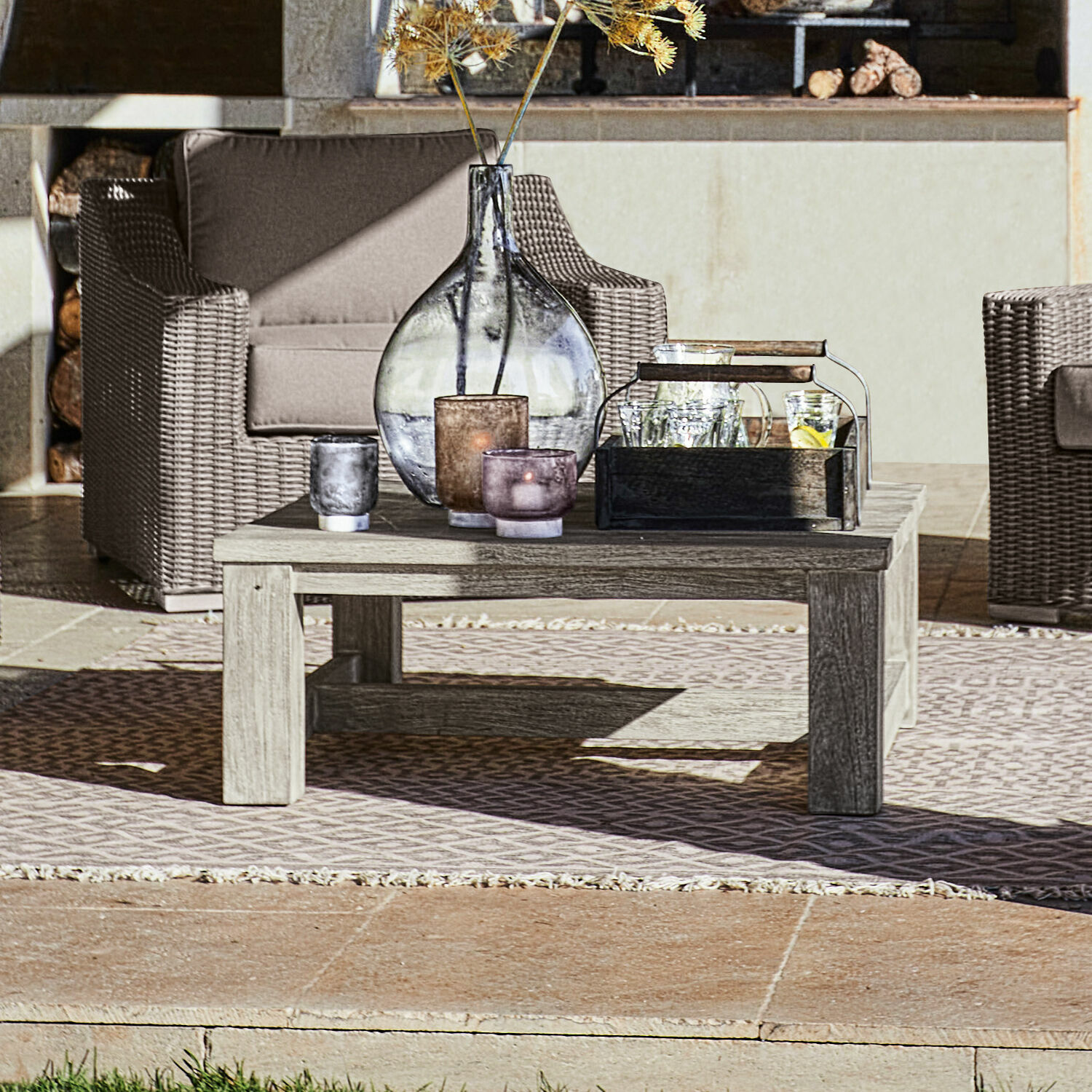 Table basse Malden Table basse en bois clair sur terrasse avec bougies décoratives et vase, mobilier de jardin en rotin