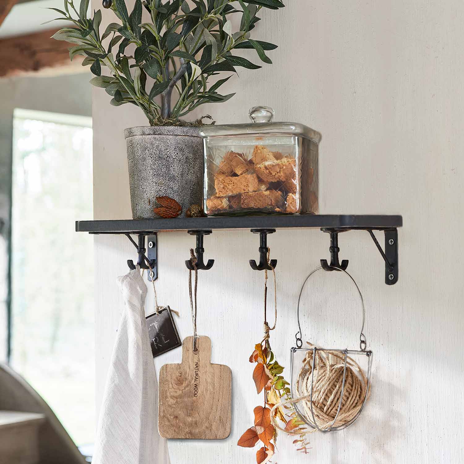 Zwart metalen wandplank met haken, bloempot met groene plant en glazen pot met koekjes