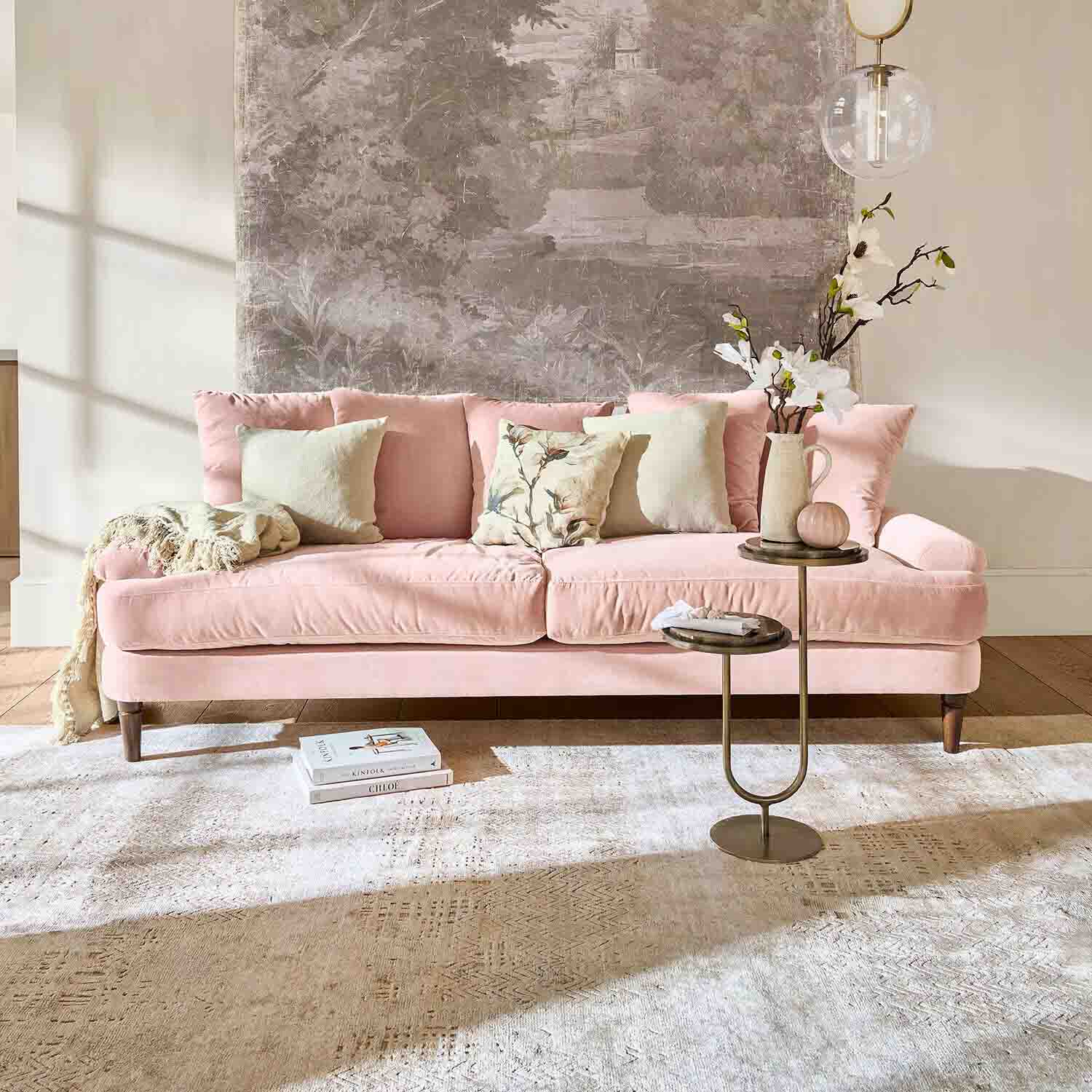 Canapé en velours rose avec coussins et table d'appoint dans un salon lumineux avec décoration murale