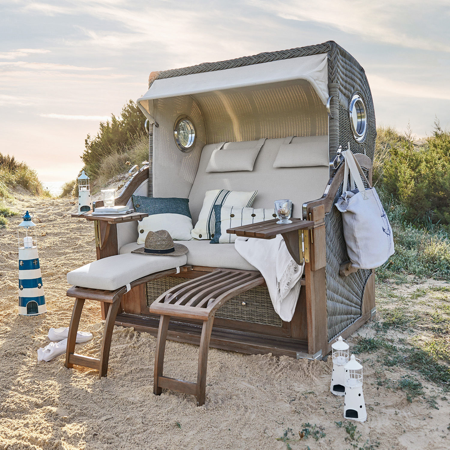 Strandkorf Clifford Beach Rieten strandstoel met beige kussen en houten voetensteunen op zand, tuinmeubilair