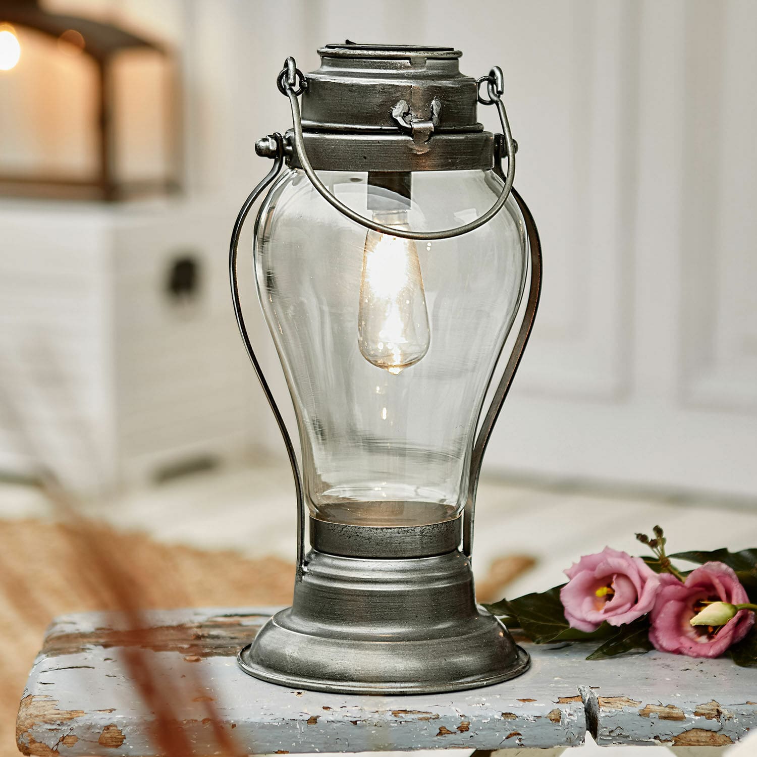 Lanterne solaire Melini Lanterne en métal avec abat-jour en verre transparent et lumière chaude sur une table en bois