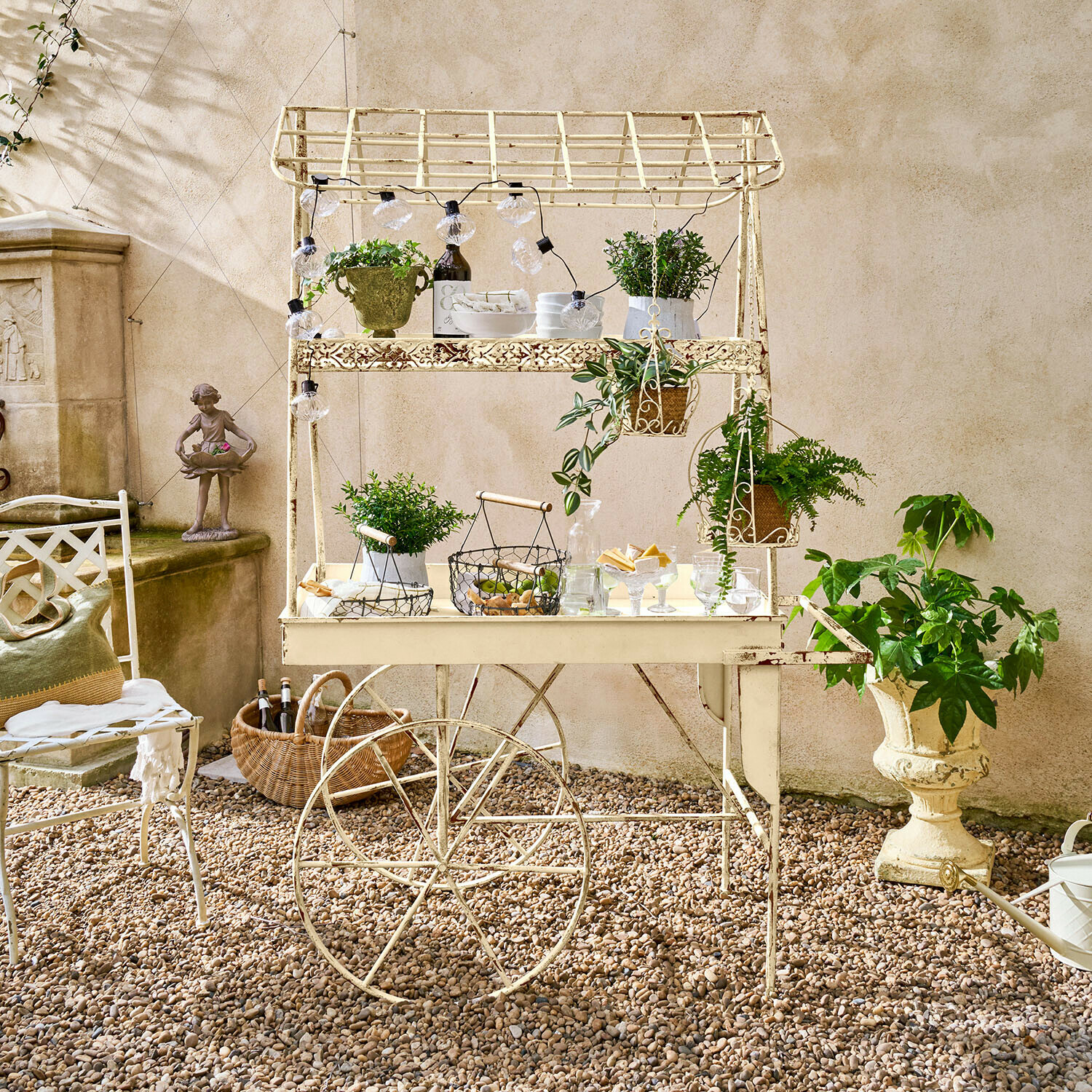 Crèmekleurige metalen tuinwagen met planten en decoraties op grindterras