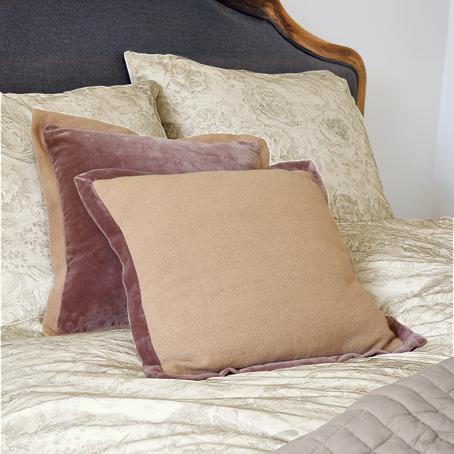 Coussins décoratifs beige et rose en velours et tissu sur lit avec linge de lit clair
