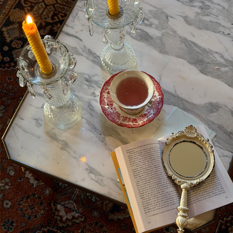 Glazen kandelaars met gele kaarsen en kopje met rood patroon op marmeren tafel met boek en handspiegel