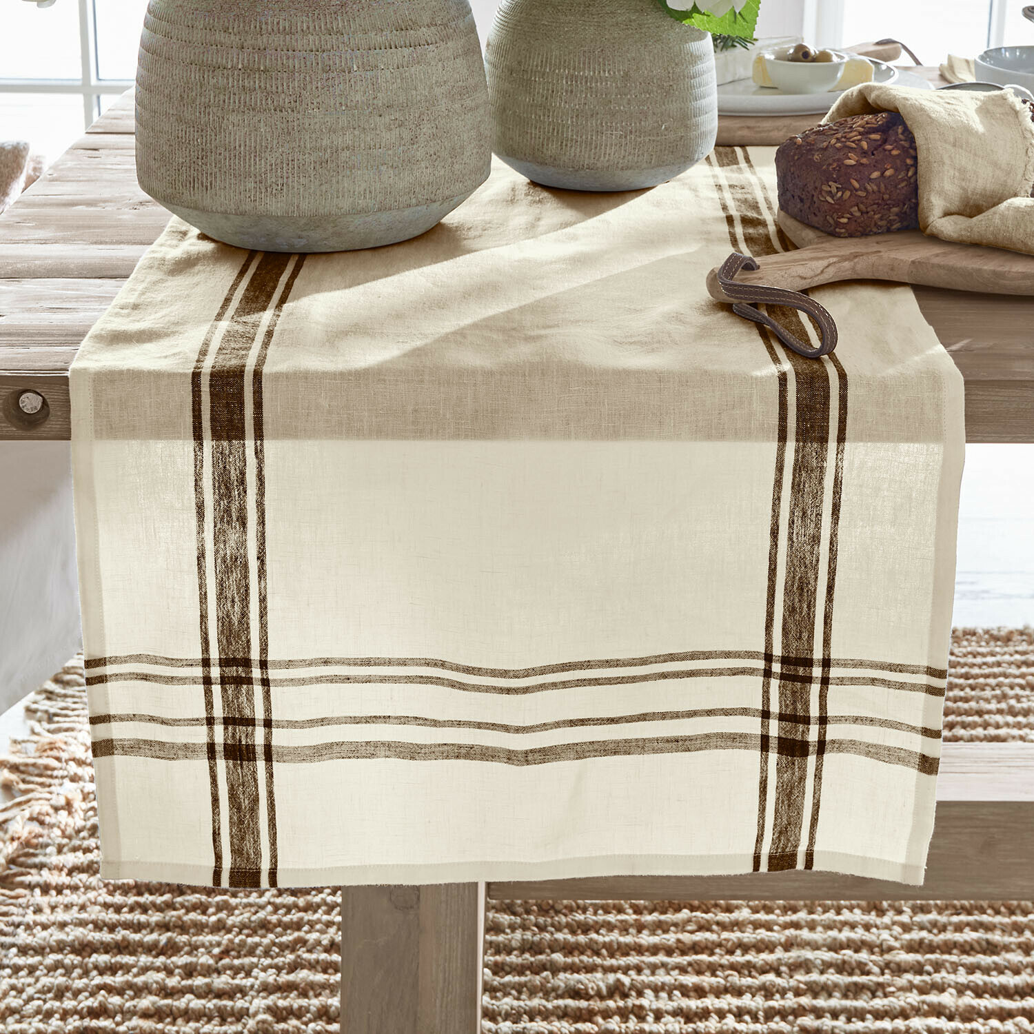 Tafelloper Ellory Beige linnen tafelloper met bruine strepen op houten tafel, gedecoreerd met brood en servies
